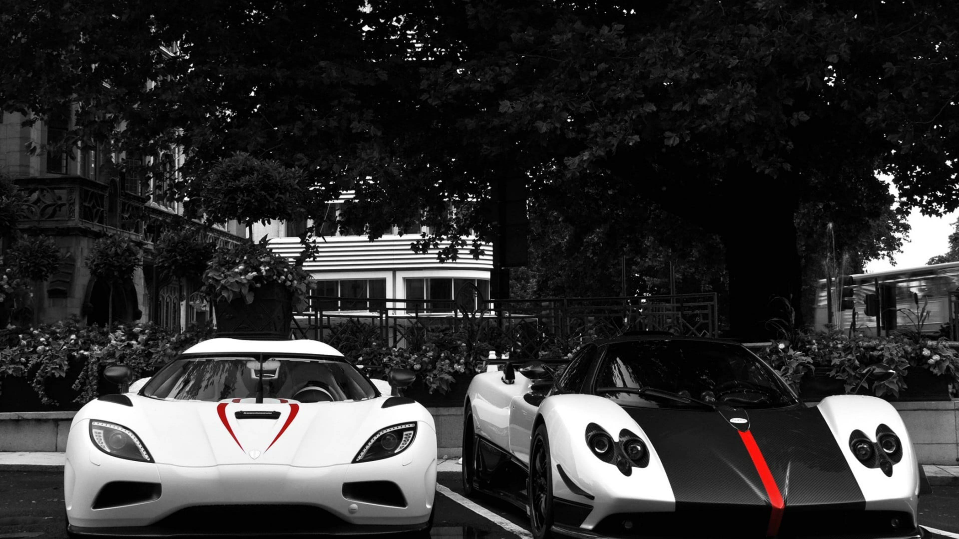 Pagani 桌布 壁紙 — 兩輛時尚的白色超級跑車帶有紅色點綴，停放在綠樹成蔭的單色城市環境中。