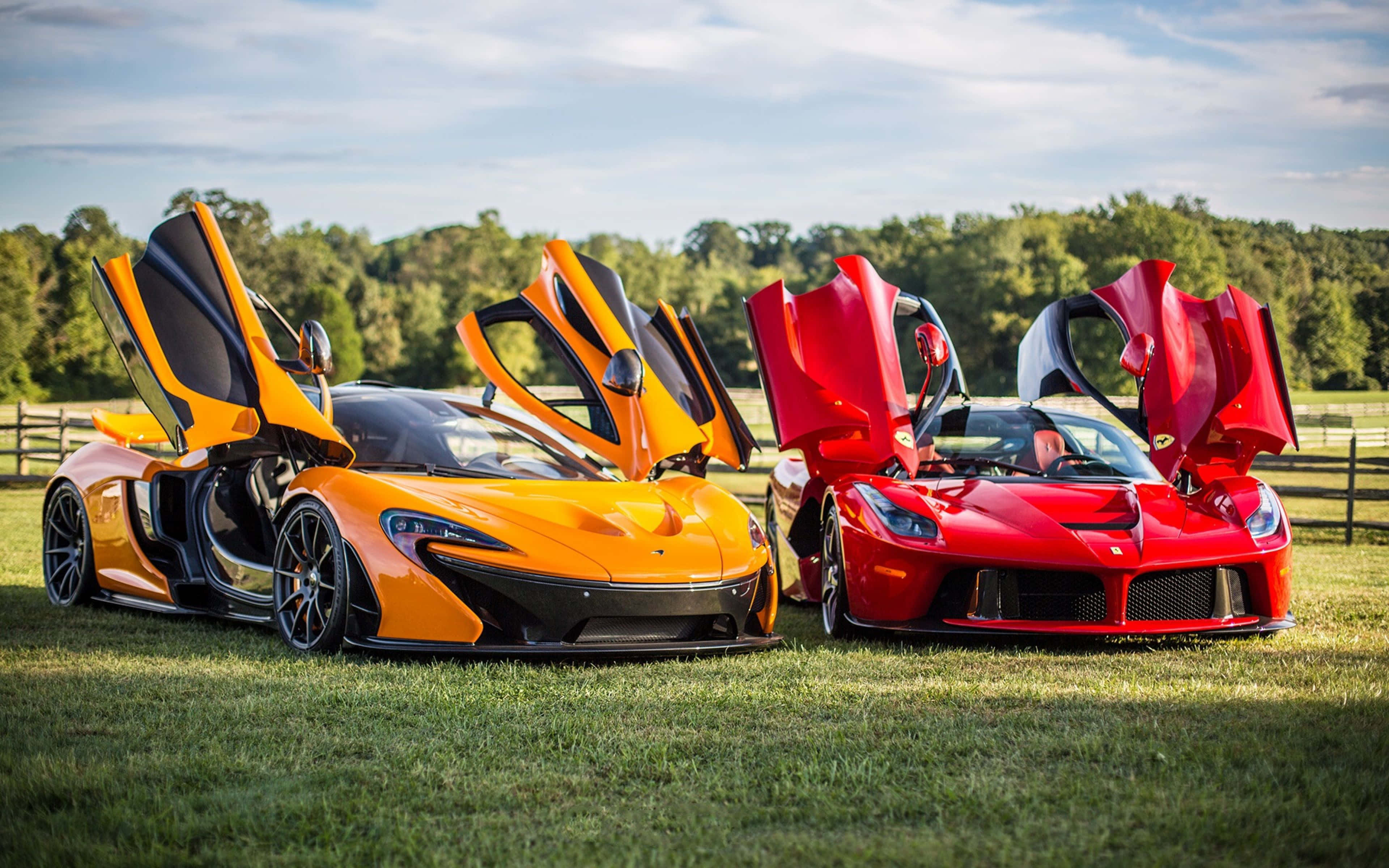 Ferrari Laferrari 桌布 壁紙 — 兩輛時尚超級跑車，橙色McLaren和紅色Ferrari，車門打開，停在晴朗天空下的草地上。