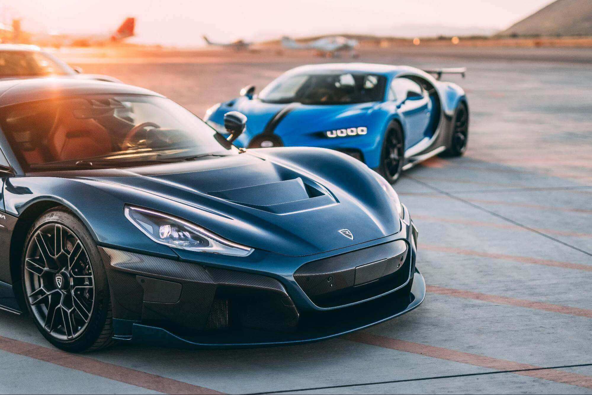 Rimac 桌布 壁紙 — 兩輛時尚超跑，一輛深藍色和一輛亮藍色，停在沐浴在金色夕陽下的機場停機坪上。