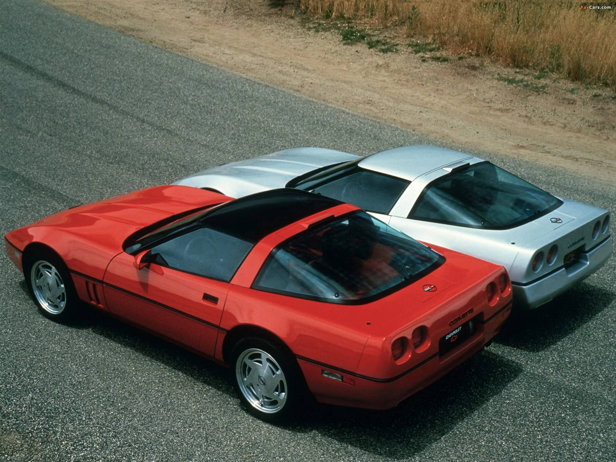 corvette 桌布 壁紙 — 兩輛時尚跑車，一輛鮮紅色和一輛金屬銀色，並排停放在陽光普照的柏油路上。