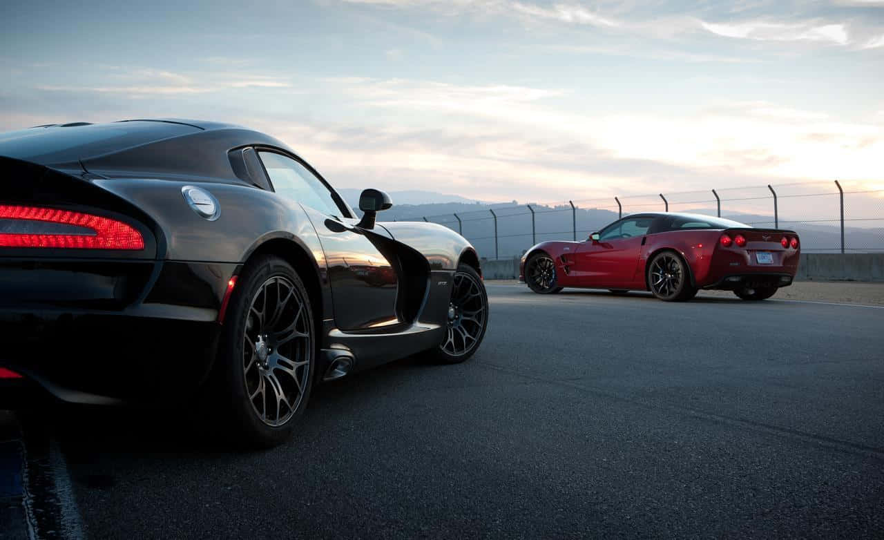 Dodge 桌布 壁紙 — 兩輛時尚跑車一輛消光黑色Dodge Viper和一輛鮮紅色Chevrolet Corvette停在黃昏的瀝青賽道上，遠處山巒在柔和天空下。