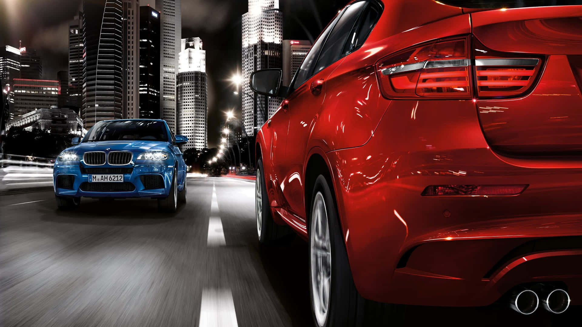 Bmw X6 M 桌布 壁紙 — 兩輛時尚跑車在霓虹燈閃爍的夜晚城市中飛馳，背後是高聳入雲的摩天大樓閃閃發光。