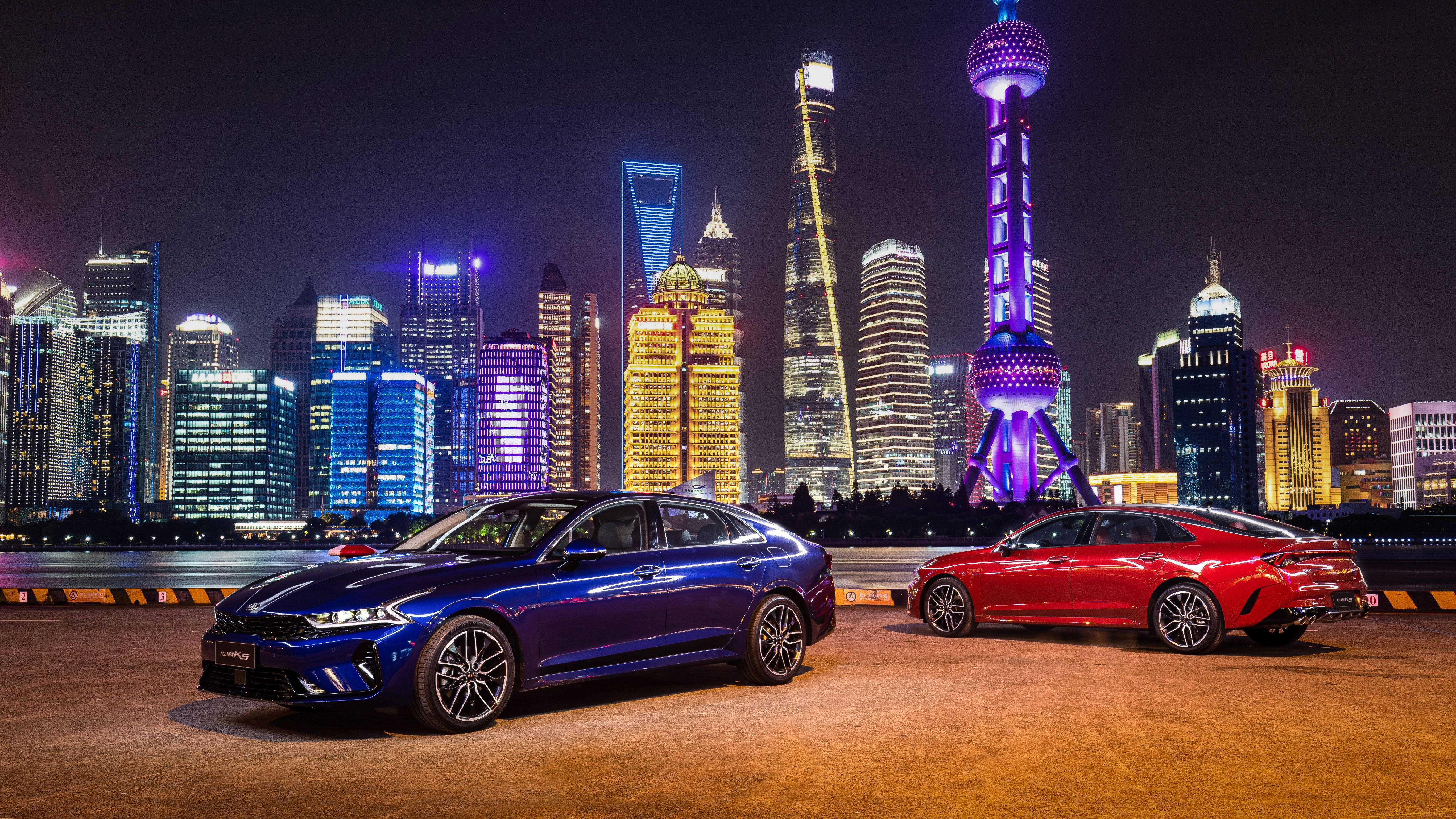 Shanghai 桌布 壁紙 — 兩輛時尚轎車在夜晚的城市燈光下，映襯著上海標誌性的璀璨天際線。