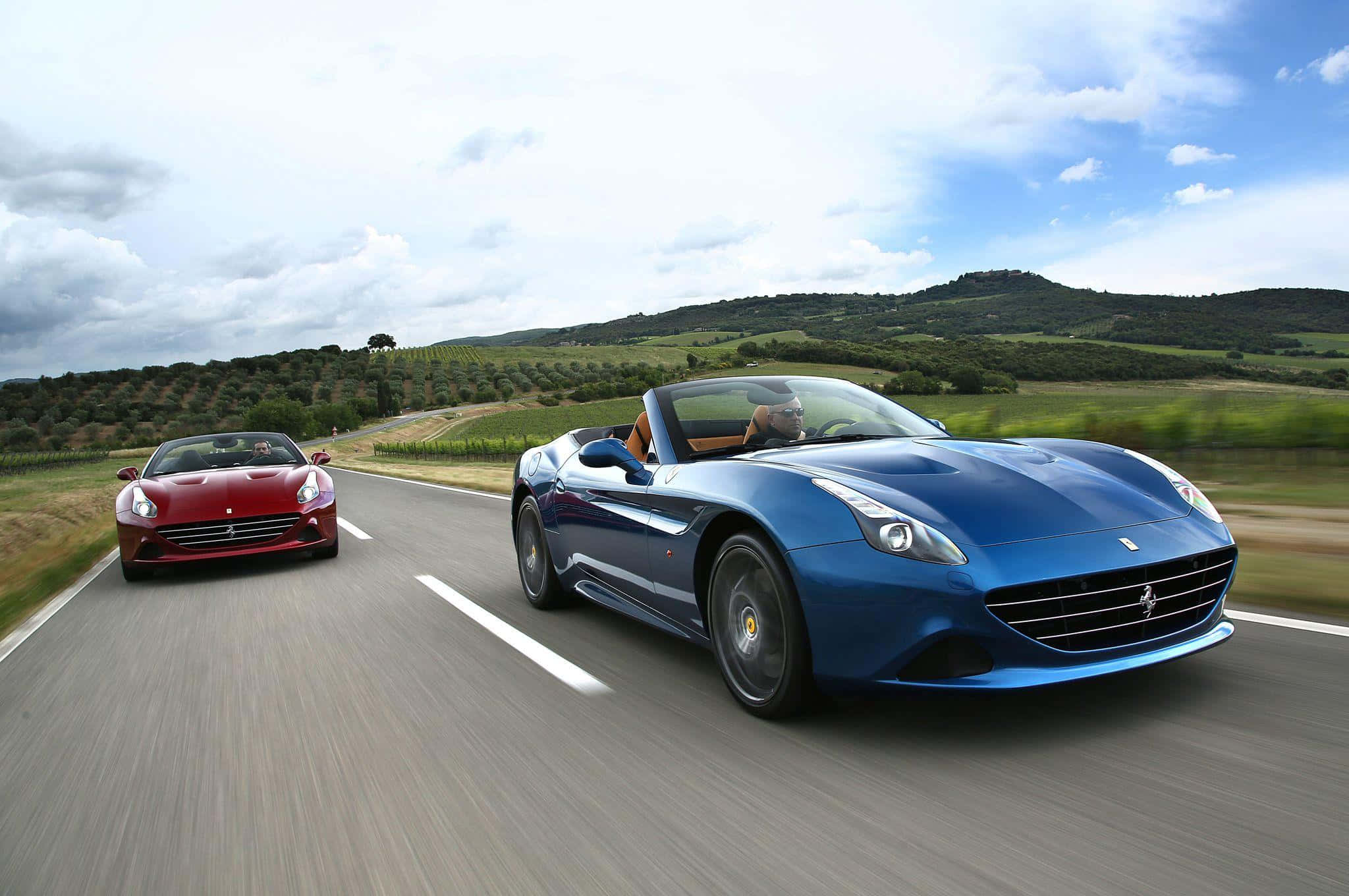 Ferrari California T 桌布 壁紙 — 兩輛法拉利敞篷車在部分多雲的天空下沿著蜿蜒的鄉村道路競速。