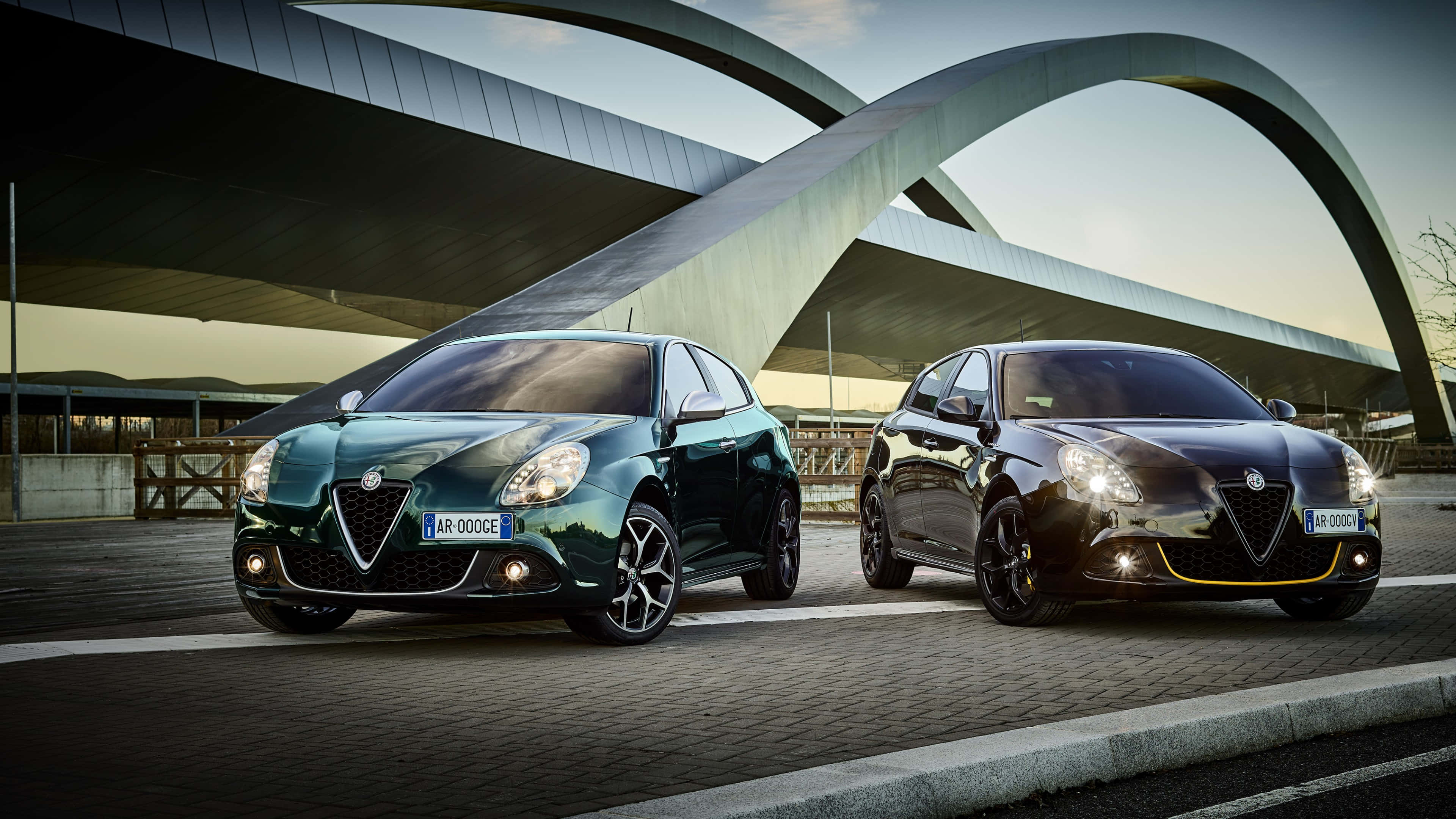 Alfa Romeo Giulietta 桌布 壁紙 — 兩輛流線型的愛快羅密歐汽車在未來風格的彎曲金屬結構下，於黃金時刻的光芒中閃耀。
