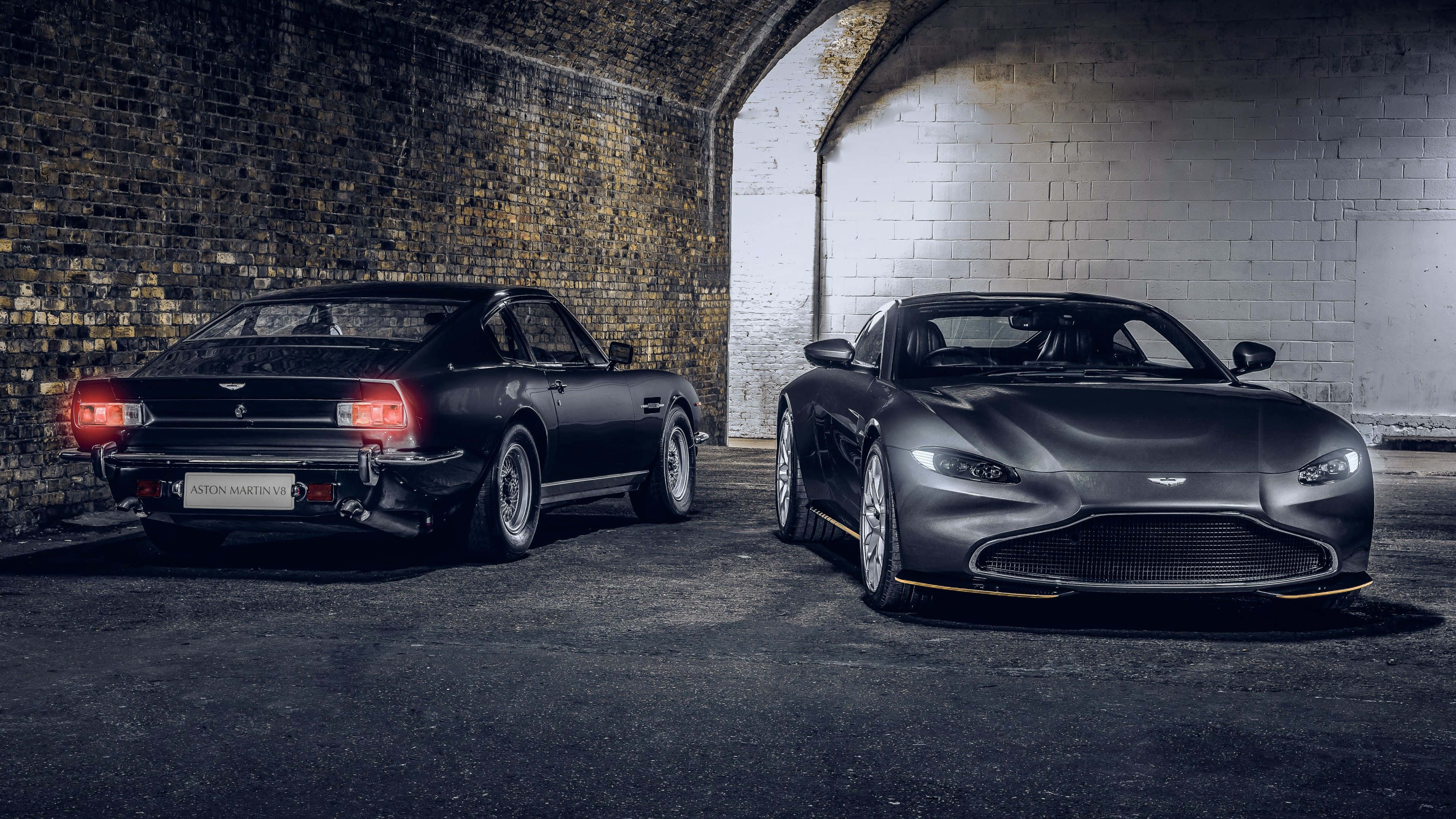 Aston Martin V12 Vantage 桌布 壁紙 — 兩輛消光黑色的Aston Martin跑車停放在光線昏暗的磚砌隧道中，帶有戲劇性的燈光效果。