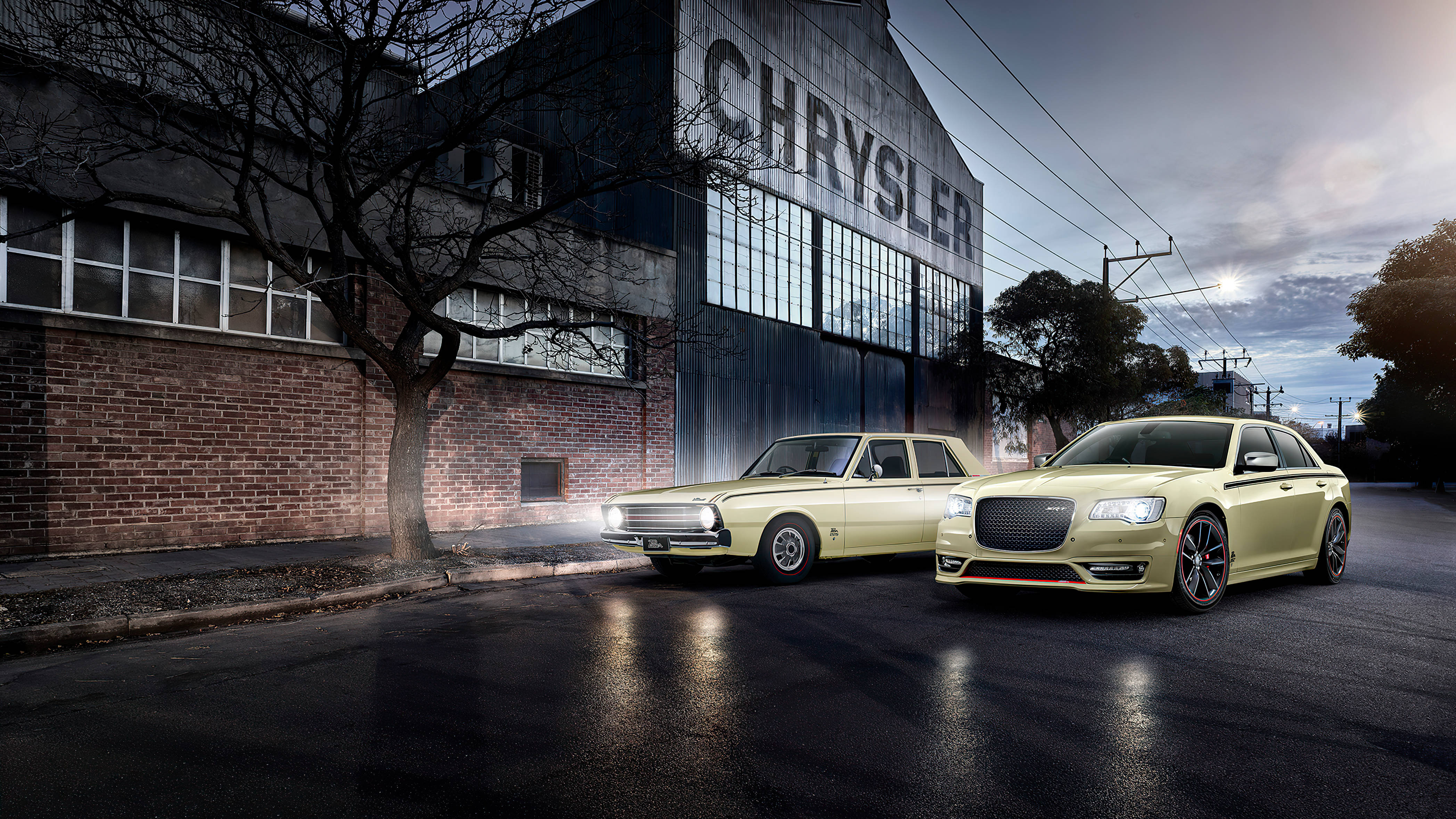 Chrysler 桌布 壁紙 — 兩輛淡黃色克萊斯勒轎車在暮色燈光下閃閃發光，旁邊是一座歷史悠久的工廠，側面刻有「CHRYSLER」字樣。