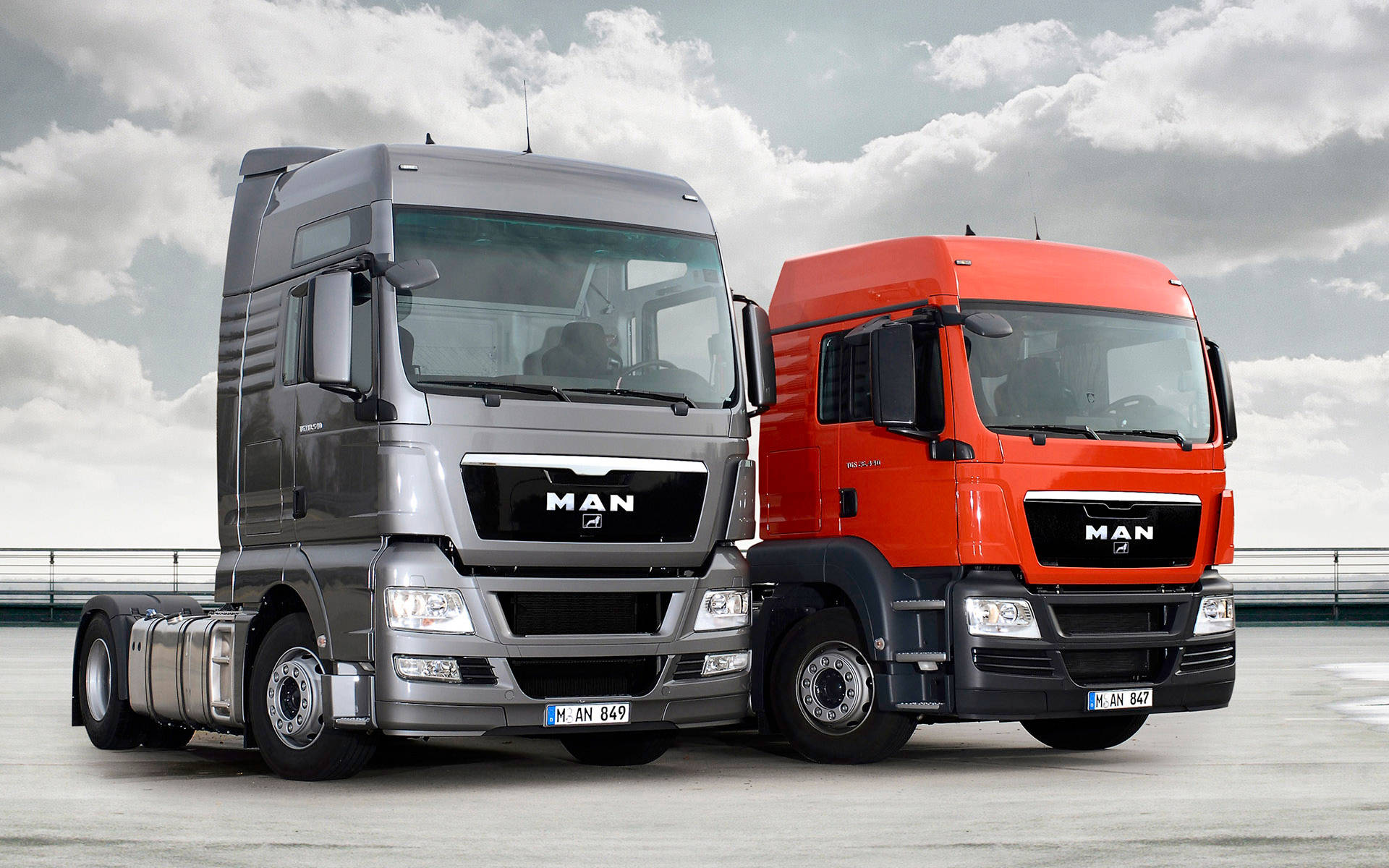 Trucks 桌布 壁紙 — 兩輛現代MAN卡車，一輛銀色一輛橙色，並排停放在多雲的天空下。