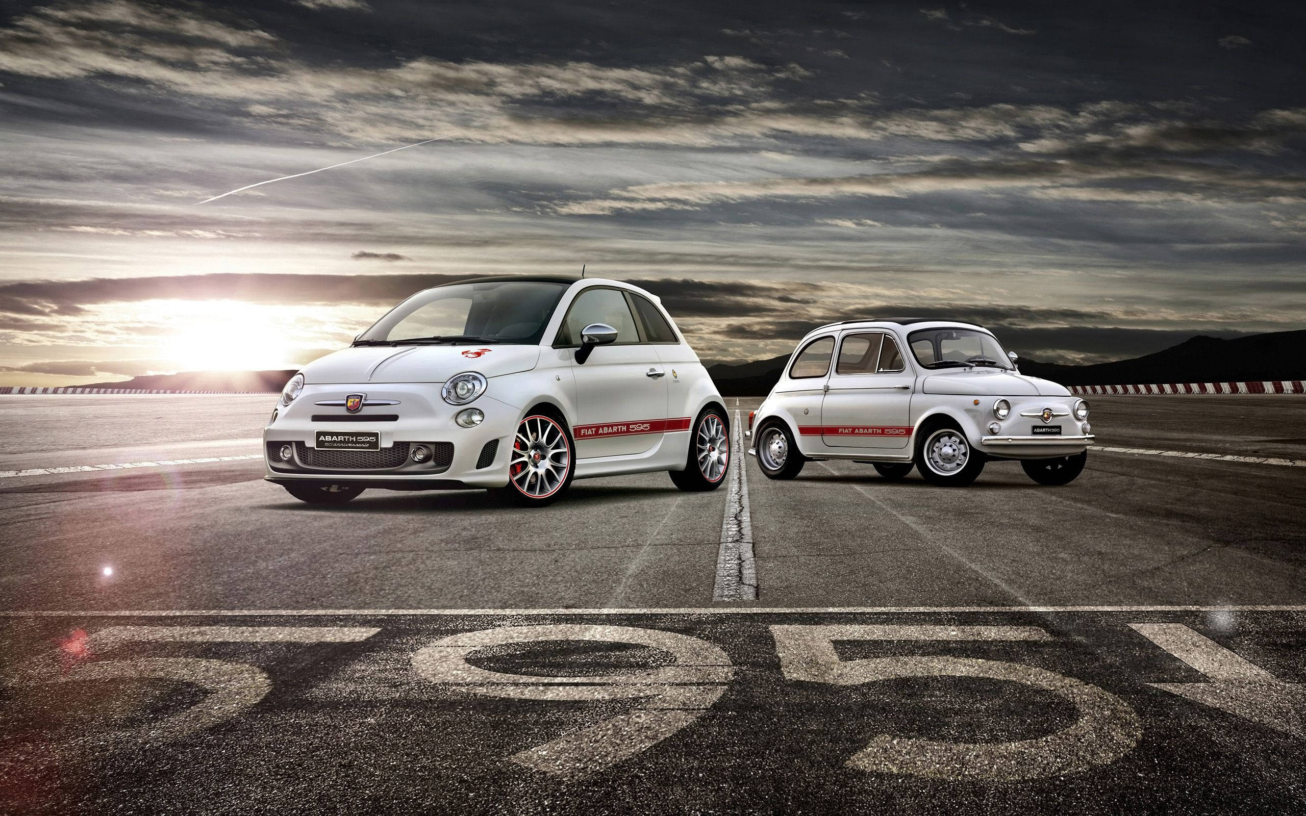 Fiat 桌布 壁紙 — 兩輛白色Fiat 500汽車在賽車道上相對，瀝青上塗有'1951'，背景是戲劇性的日落天空。