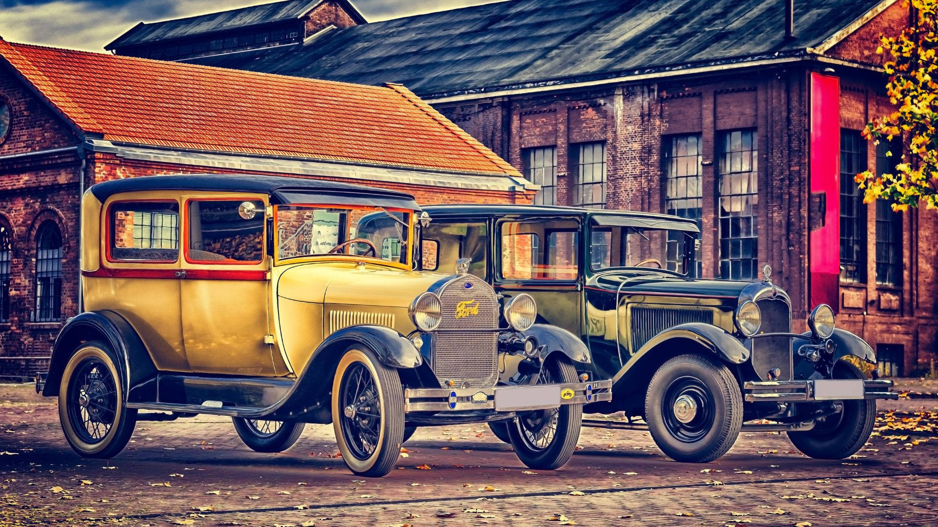 Retro 桌布 壁紙 — 兩輛福特老爺車停泊在磚砌建築前的鵝卵石街道上，周圍散落著秋葉。
