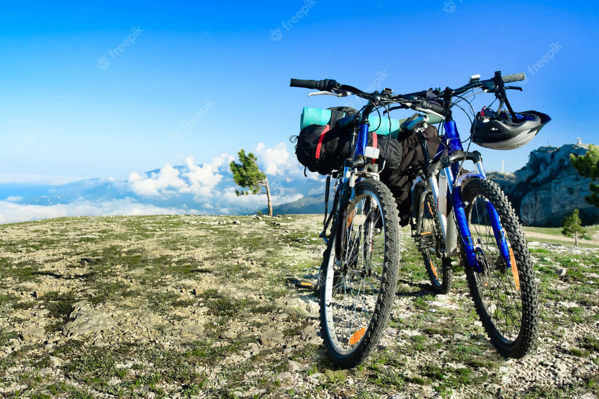 Mountain Bike 桌布 壁紙 — 兩輛藍色登山自行車裝有裝備包，停放在岩石山頂上，俯瞰雲海和遠山，天空清澈湛藍。