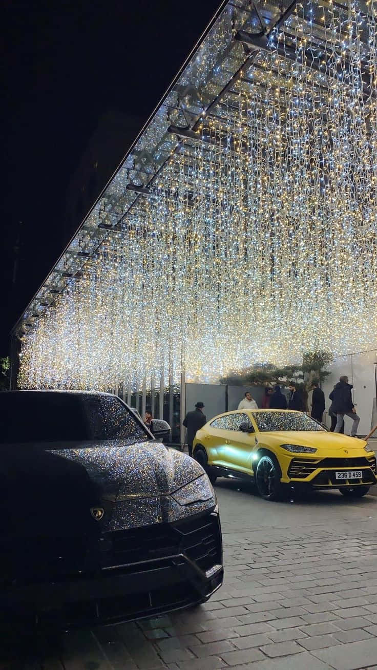 Family Car 桌布 壁紙 — 兩輛豪華SUV在夜間城市活動中，在懸掛的仙女燈的耀眼天篷下閃閃發光。