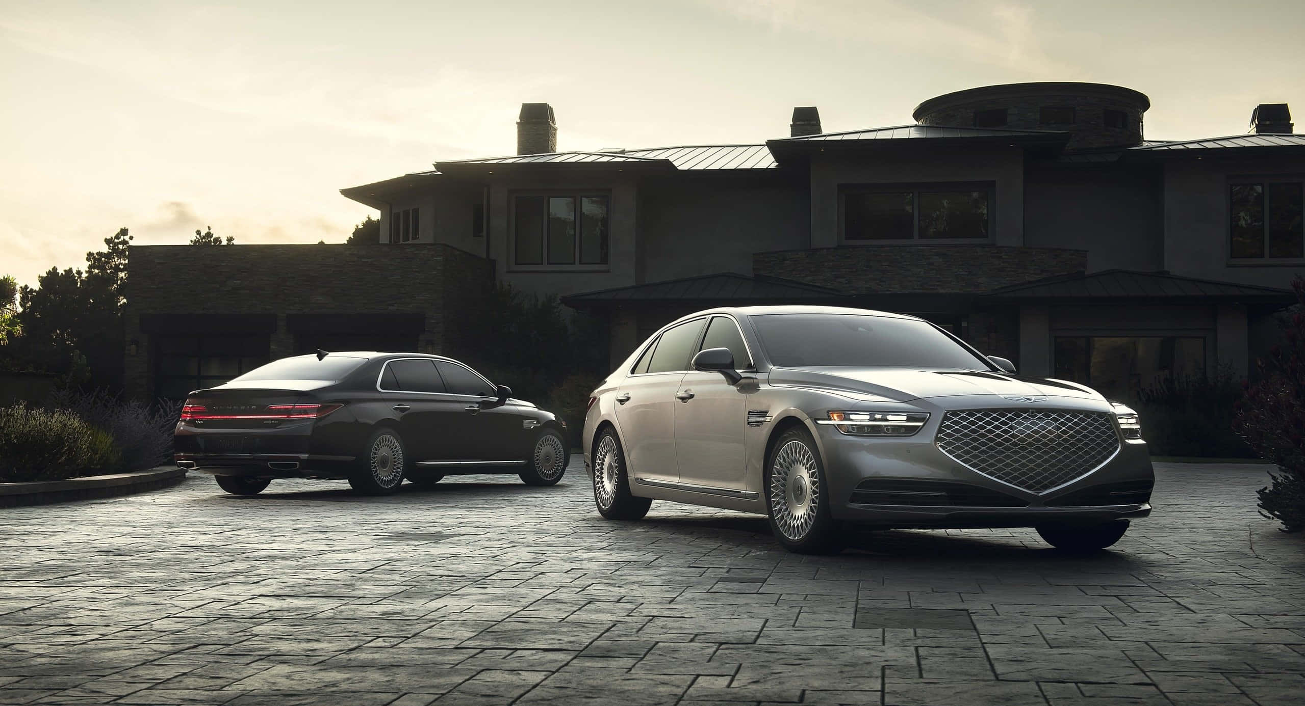 Genesis G90 桌布 壁紙 — 兩輛豪華轎車停放在現代房屋前的石頭車道上，正值黃金時刻。