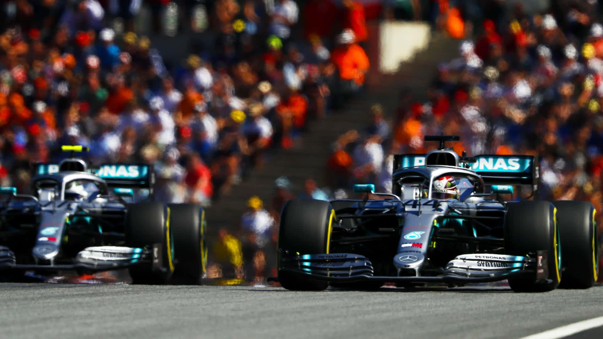 Formula 1 桌布 壁紙 — 兩輛賓士一級方程式賽車在陽光明媚的賽道上並排競速，背景是模糊的觀眾。