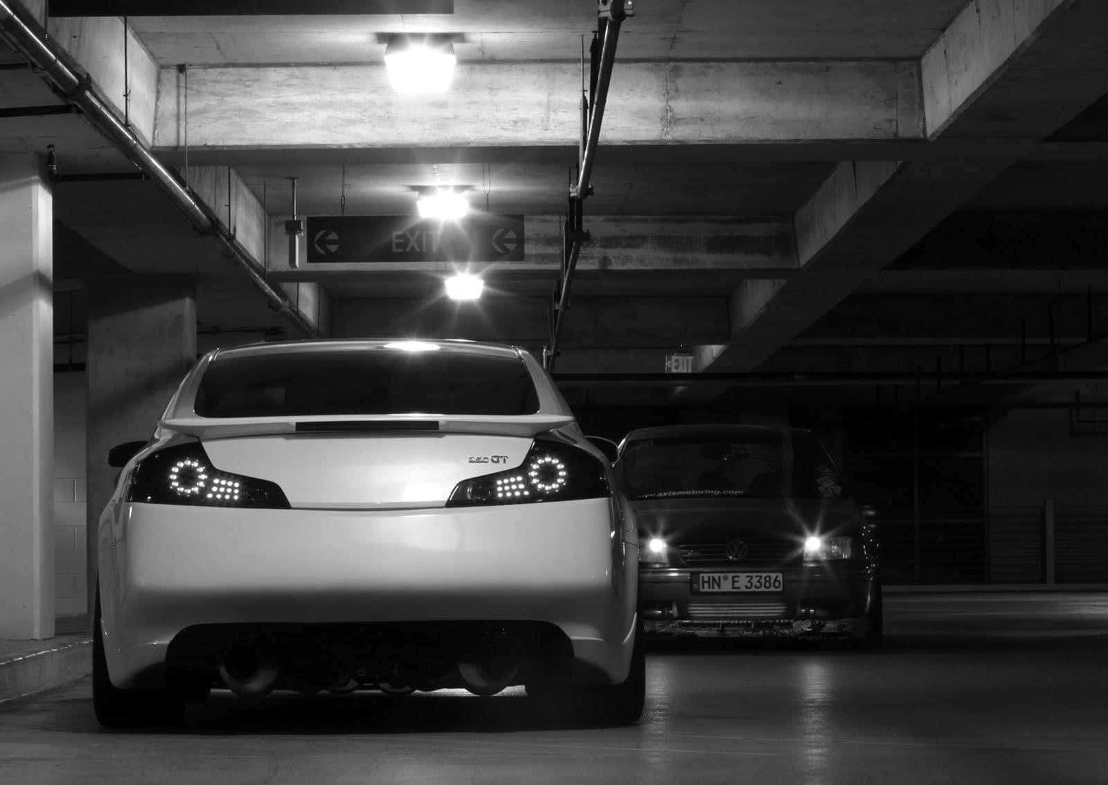Infiniti G35 桌布 壁紙 — 兩輛車停在光線昏暗的地下車庫，車頭燈發光，頭頂有出口標誌。