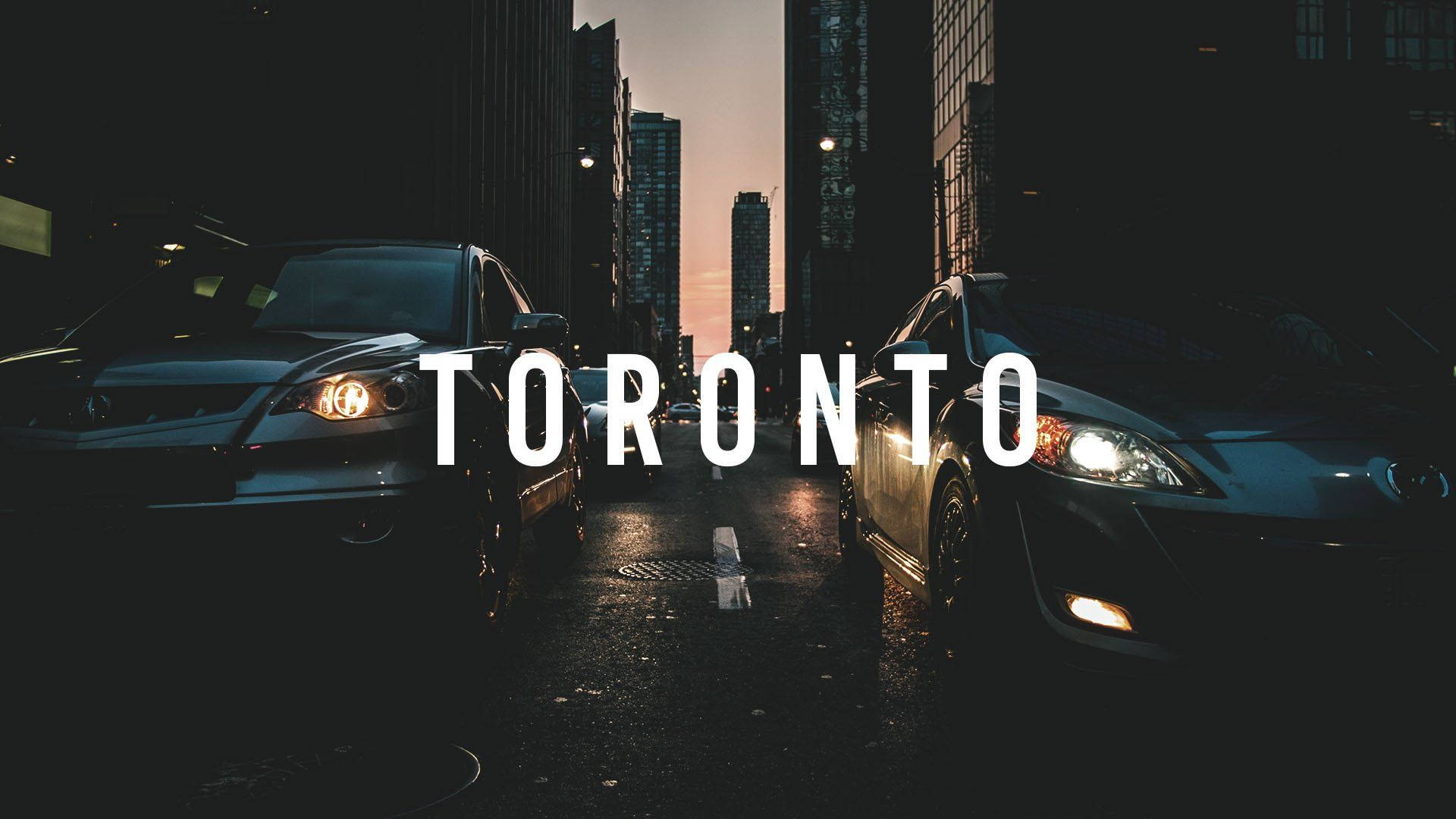 Toronto 桌布 壁紙 — 兩輛車在黃昏時分的濕漉漉城市街道上相對而行，高樓大廈和「TORONTO」文字疊加。