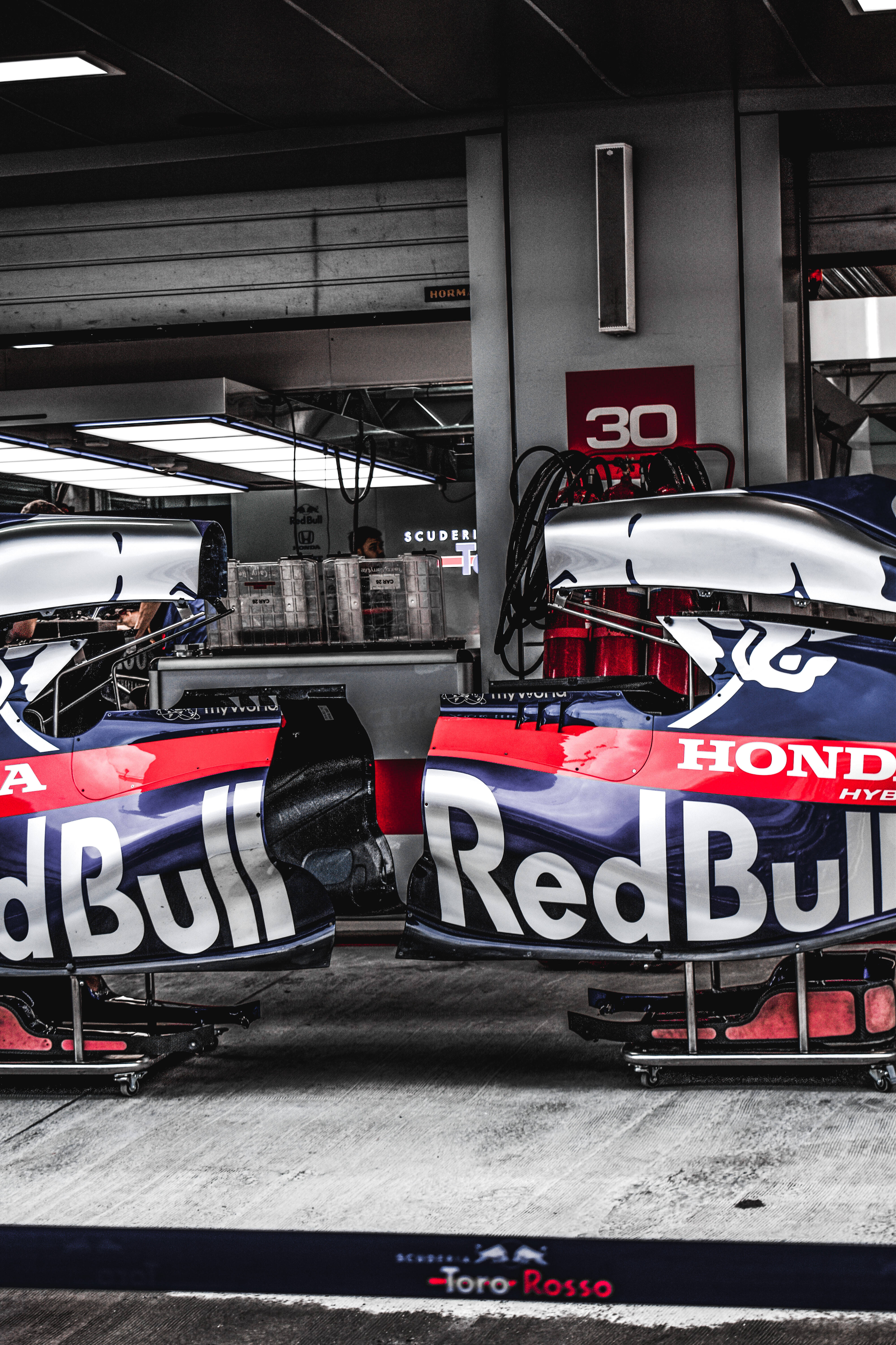 Red Bull 桌布 壁紙 — 兩輛配備本田引擎的紅牛一級方程式賽車停在維修區車庫，上方是明亮的螢光燈。