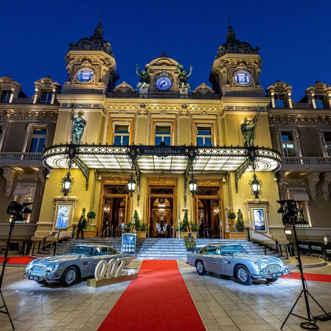 鎖屏 桌布 壁紙 — 兩輛銀色Aston Martin DB5在暮色天空下，於燈火通明的蒙地卡羅賭場兩旁排列著紅地毯。