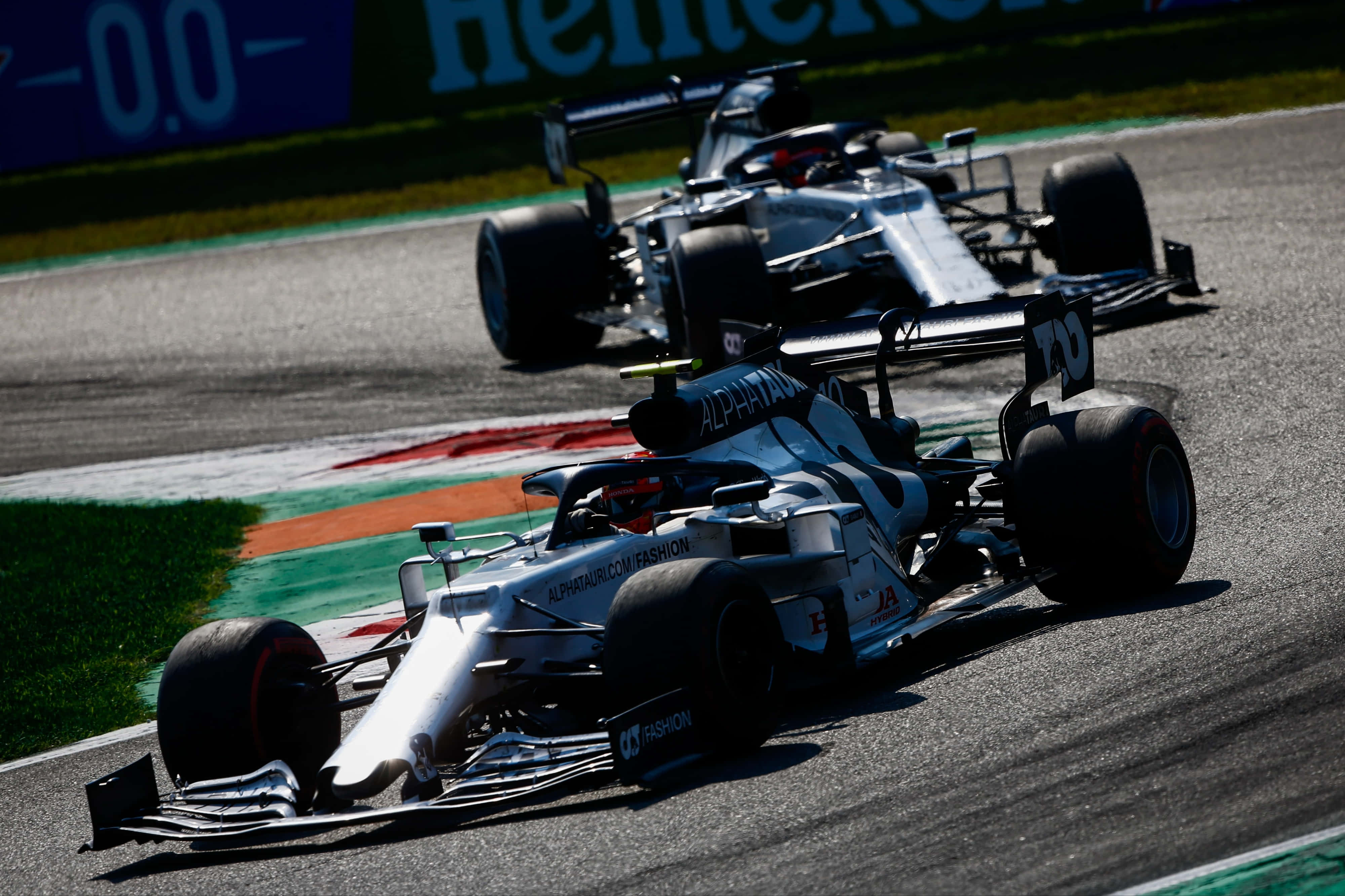 Formula One 桌布 壁紙 — 兩輛銀色一級方程式賽車在陽光明媚的賽道上緊密競速，賽道旁有鮮綠的草地和紅白相間的邊石。