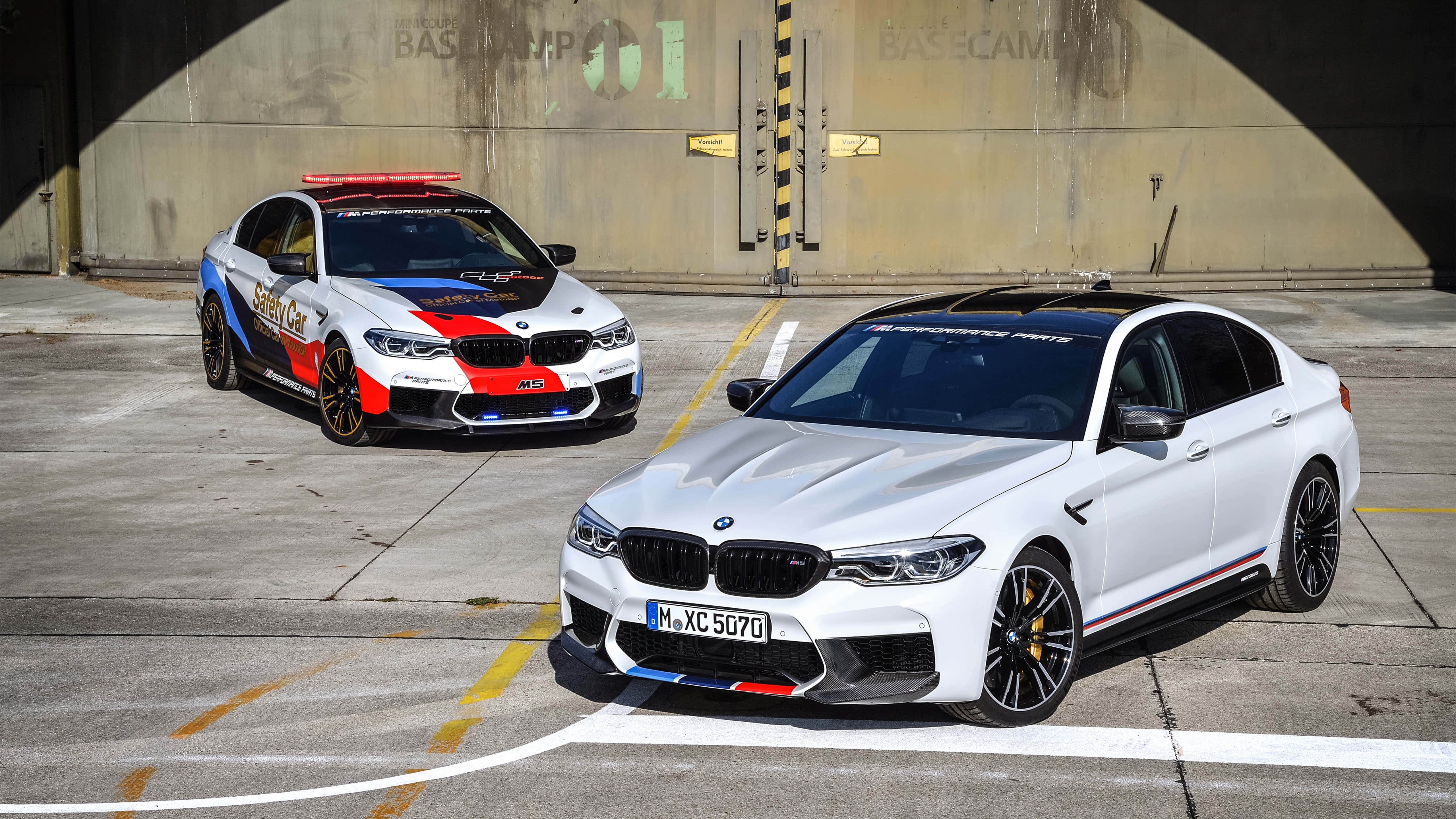 桌布 壁紙 — 兩輛高性能BMW M5停放在混凝土車庫中，一輛白色，一輛紅藍安全車。