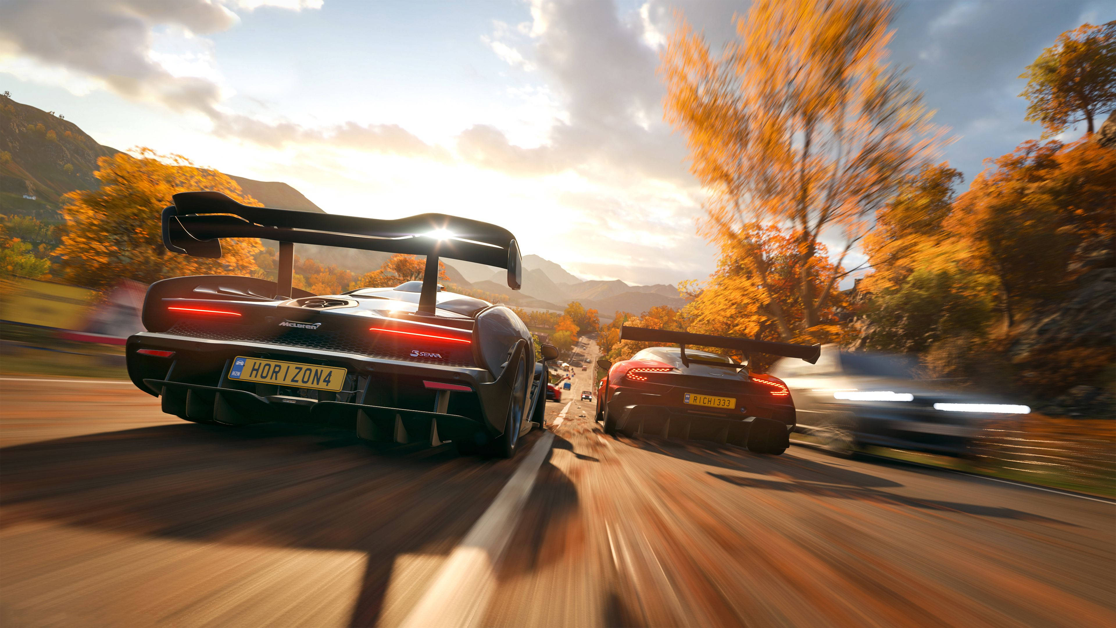 Forza Gaming 桌布 壁紙 — 兩輛高性能跑車在一條蜿蜒的秋日道路上奔馳，背景是金色的樹葉和山脈。