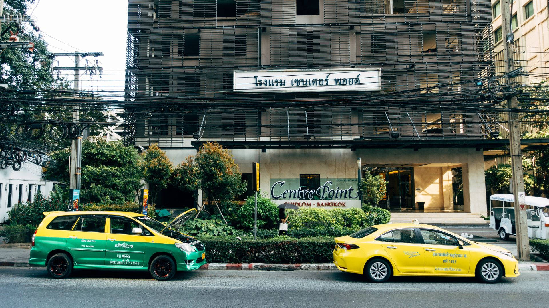 Hotel 桌布 壁紙 — 兩輛鮮黃色和綠色的計程車停泊在曼谷街頭，Centre Point酒店前面，帶有纏繞的架空電線。
