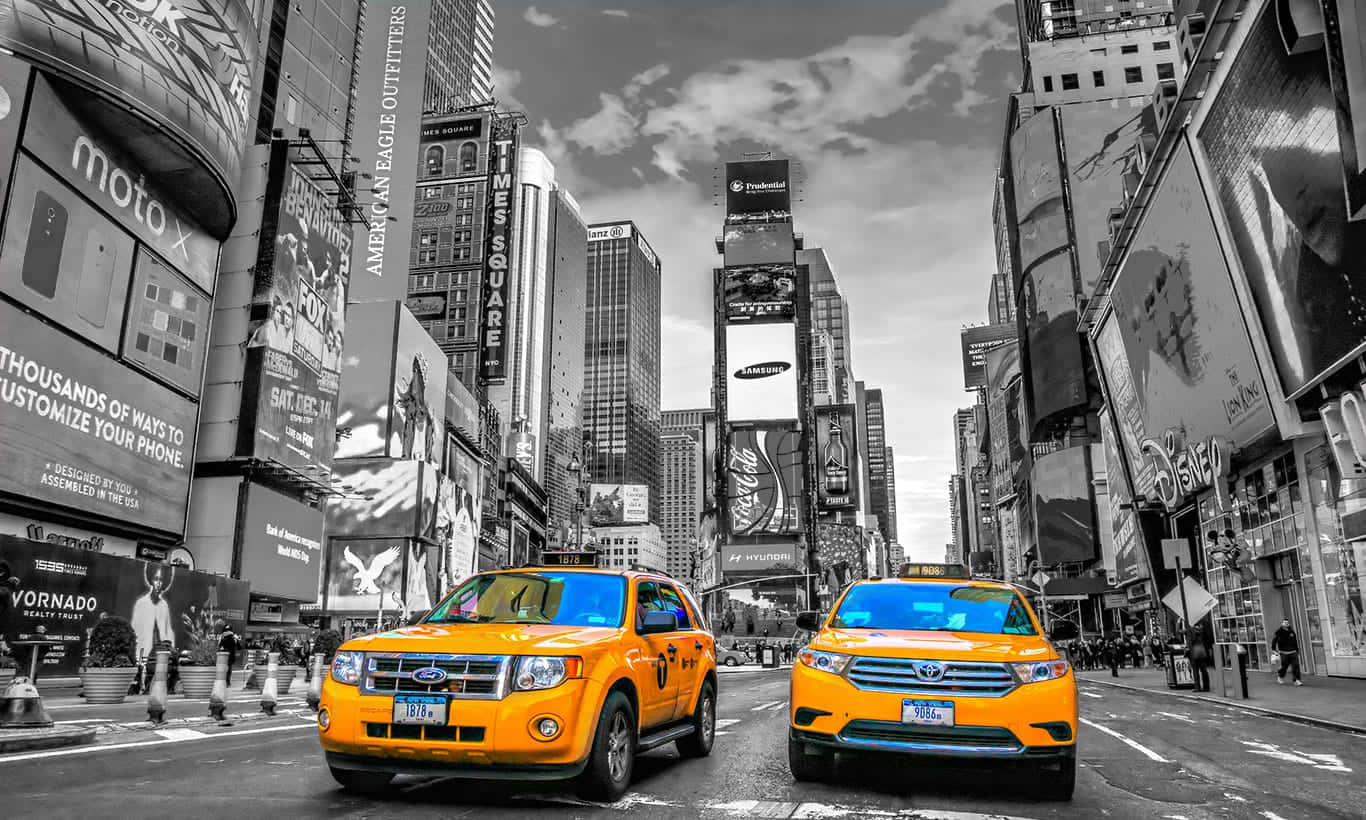 Yellow Cab 桌布 壁紙 — 兩輛鮮黃色的計程車在繁忙的時代廣場街道上行駛，周圍是高聳的廣告看板和摩天大樓，形成黑白對比。