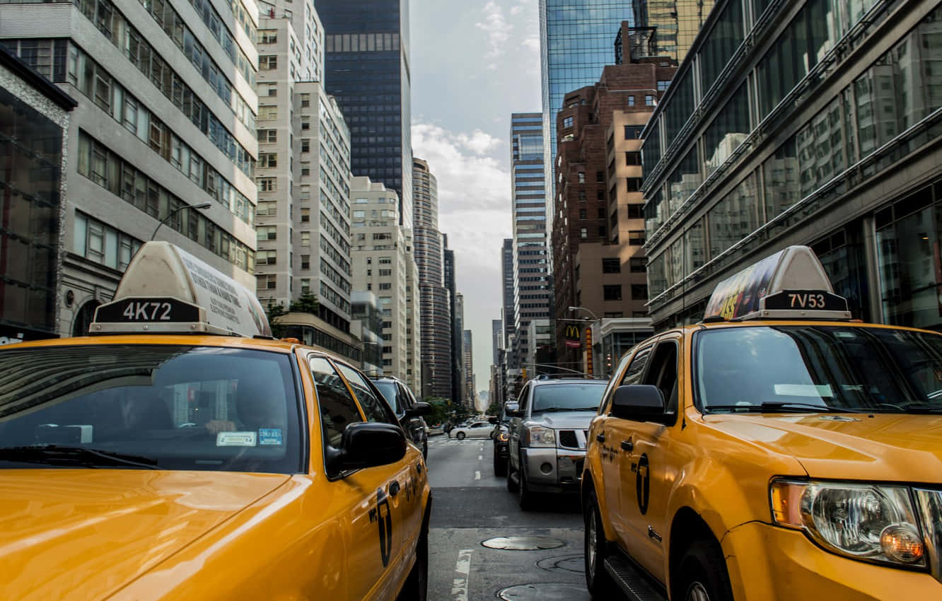 Yellow Cab 桌布 壁紙 — 兩輛黃色的士在部分多雲的天空下，夾著一條兩旁高樓林立的繁華城市街道。