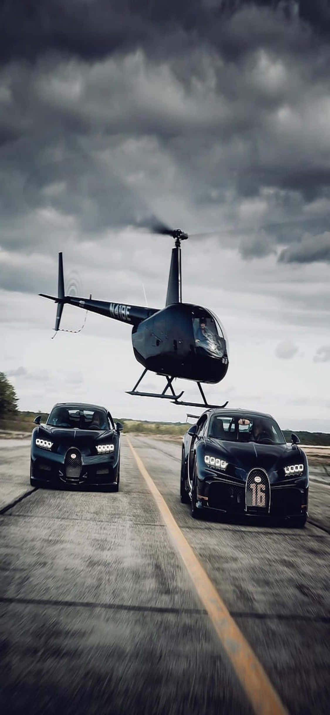 iPhone Xs Helicopters 桌布 壁紙 — 兩輛黑色Bugatti超級跑車在潮濕的道路上競速，一架黑色直升機在暴風雨的天空下盤旋於上空。