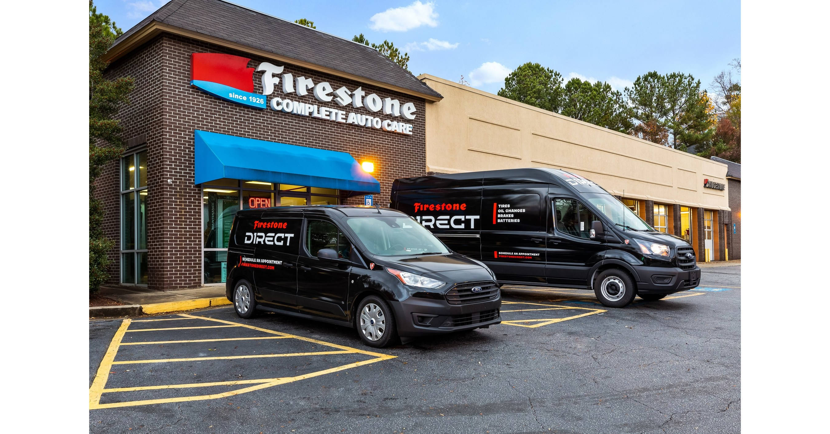 Firestone 桌布 壁紙 — 兩輛黑色Firestone Direct貨車停放在磚造汽車維修店前，天空清澈湛藍。