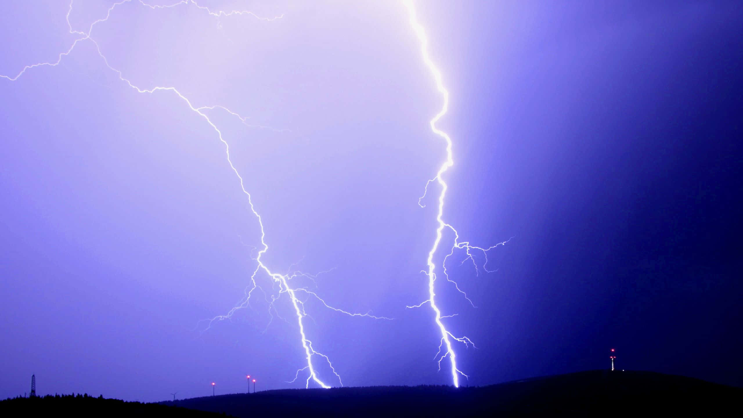 thunder 桌布 壁紙 — 兩道巨大的閃電劃破深紫色暴風雨的天空，下方是黑暗輪廓的山丘，遠處有紅燈。