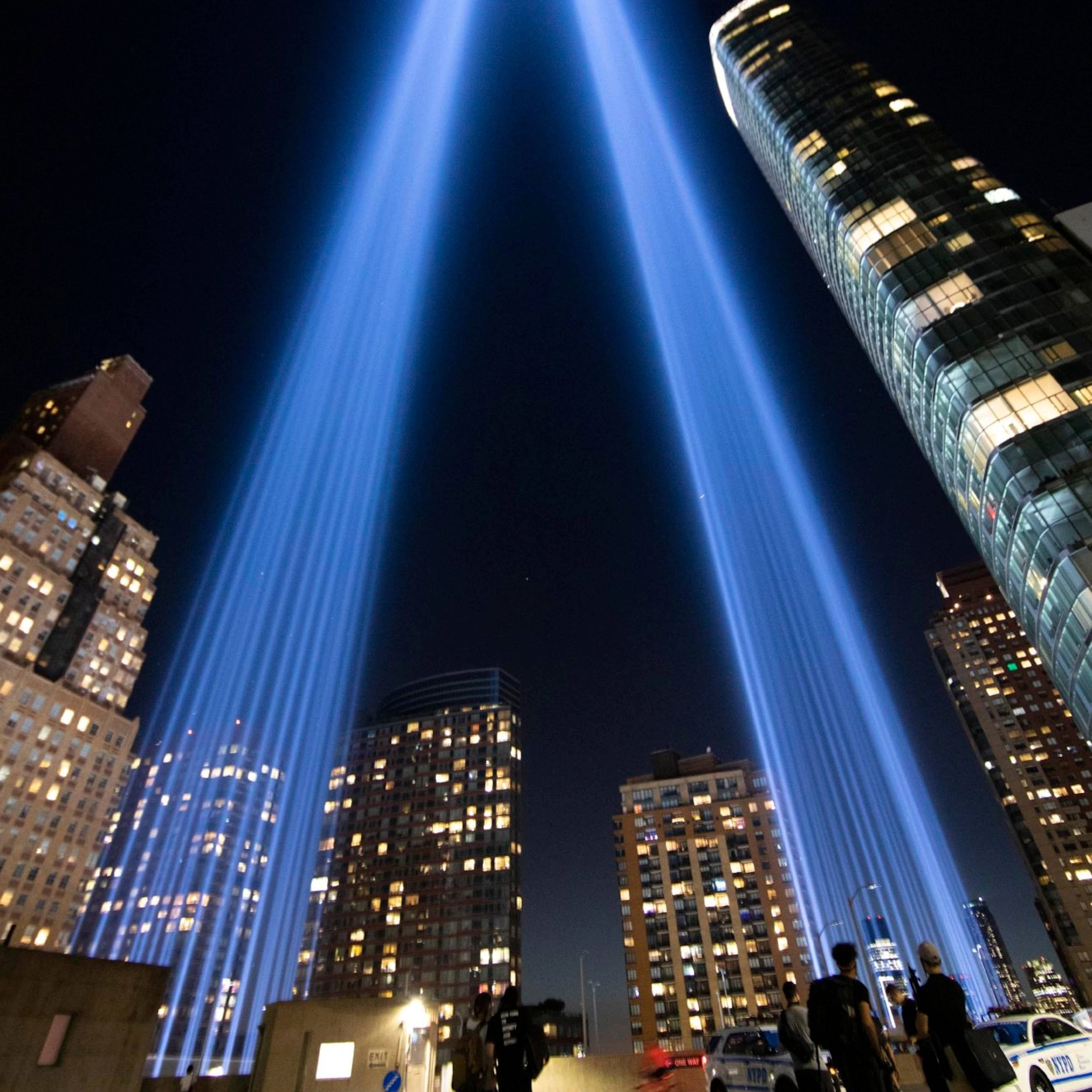911 Memorial 桌布 壁紙 — 兩道強大的藍色光束穿透高聳城市摩天大樓之間的夜空，照亮下方的城市景觀。