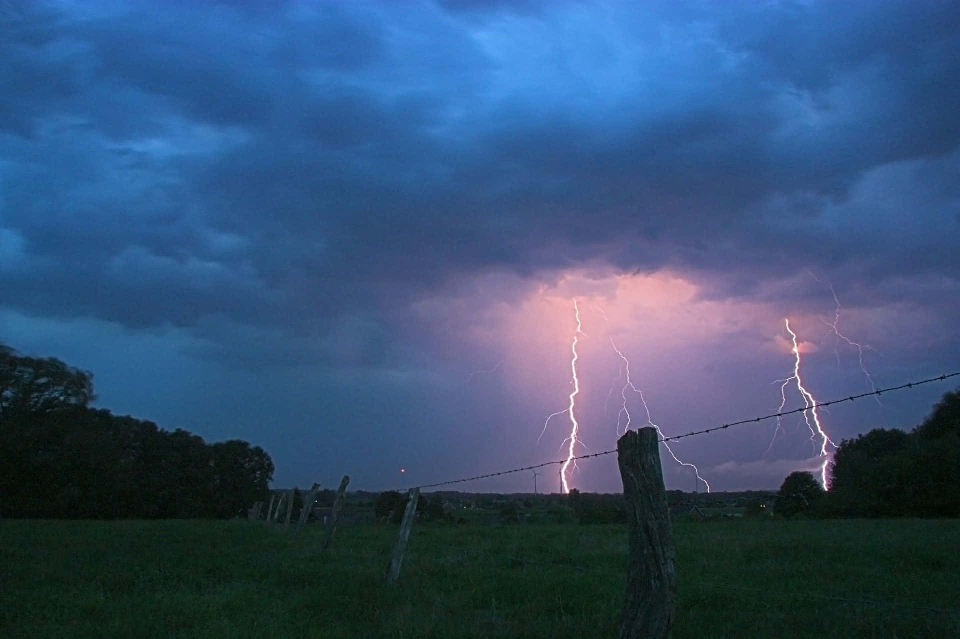 Thunderstorm 桌布 壁紙 — 兩道鋸齒狀閃電劃破風暴暮色天空，下方是帶有鐵絲網圍欄的草地。