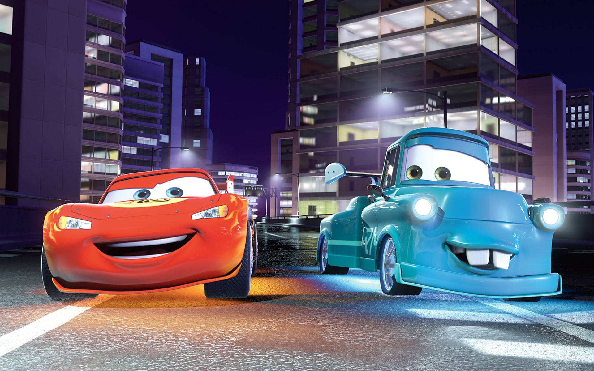 Pixar 桌布 壁紙 — 兩部動畫車閃電麥坤和拖車阿麥在夜晚濕滑的城市街道上燦爛微笑，車頭燈閃爍，背後是燈火通明的建築物。
