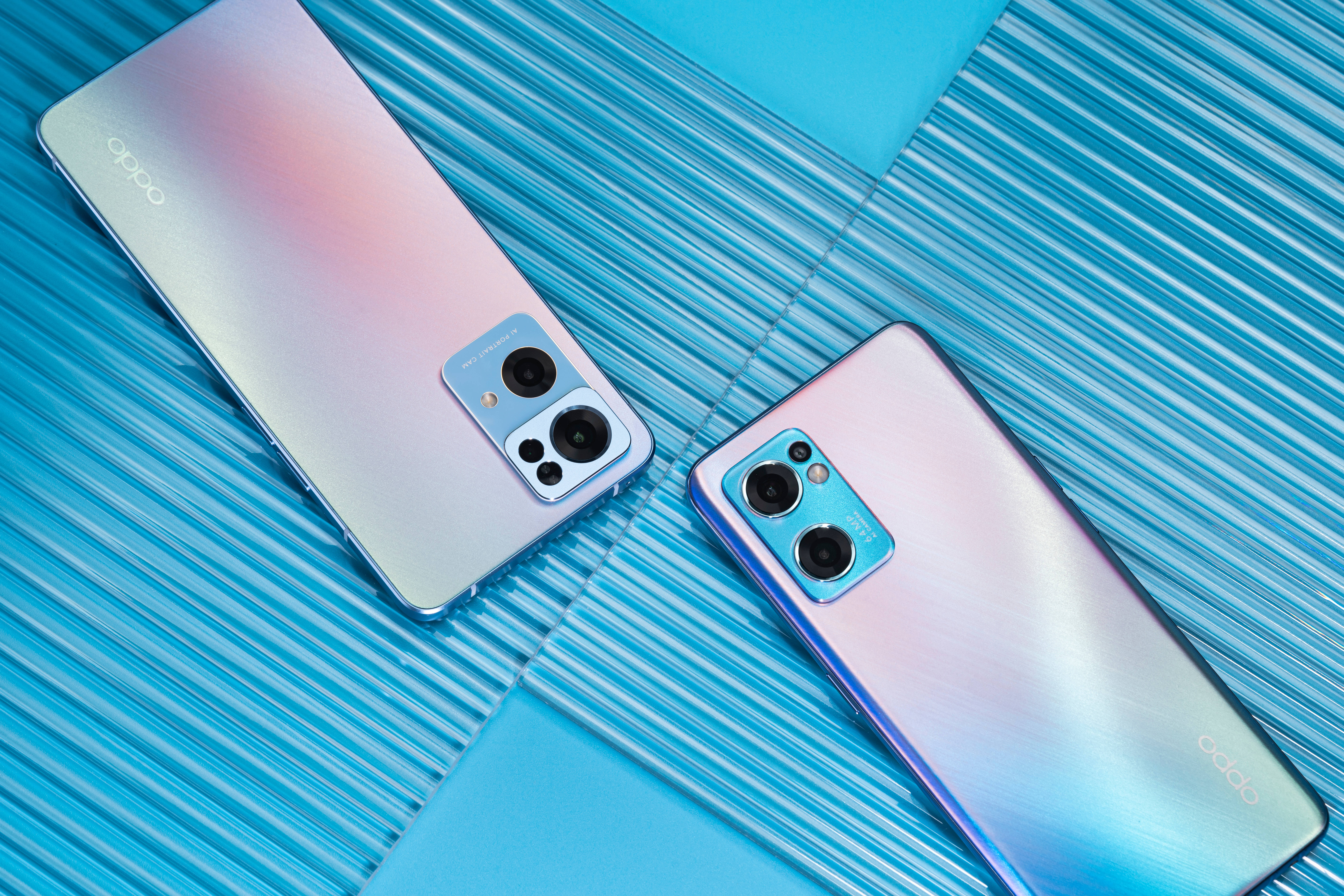 oppo 桌布 壁紙 — 兩部帶有彩虹色漸變背面的OPPO智慧型手機對角放置在帶有紋理的藍色表面上。