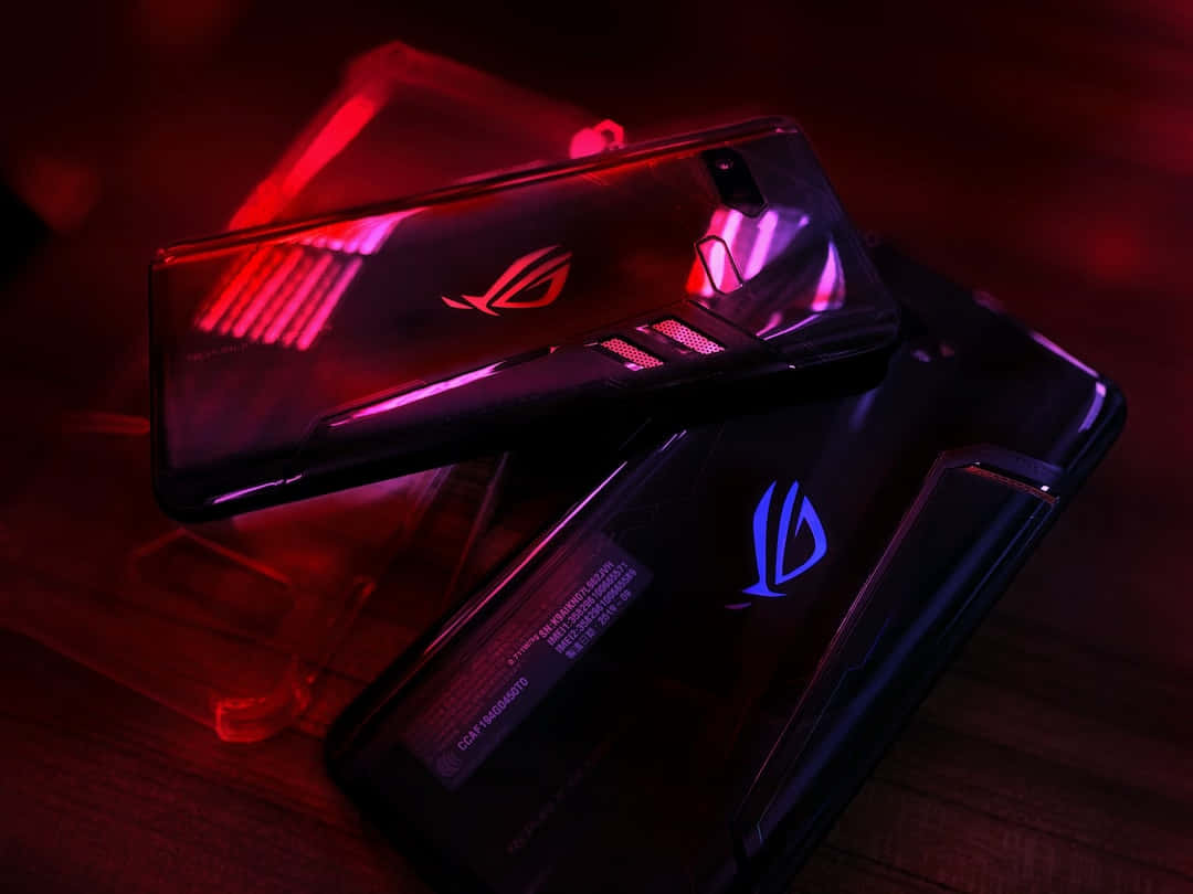 Rog 桌布 壁紙 — 兩部帶有發光RGB燈的遊戲手機放在木質表面上，在戲劇性的紅色和紫色燈光下。