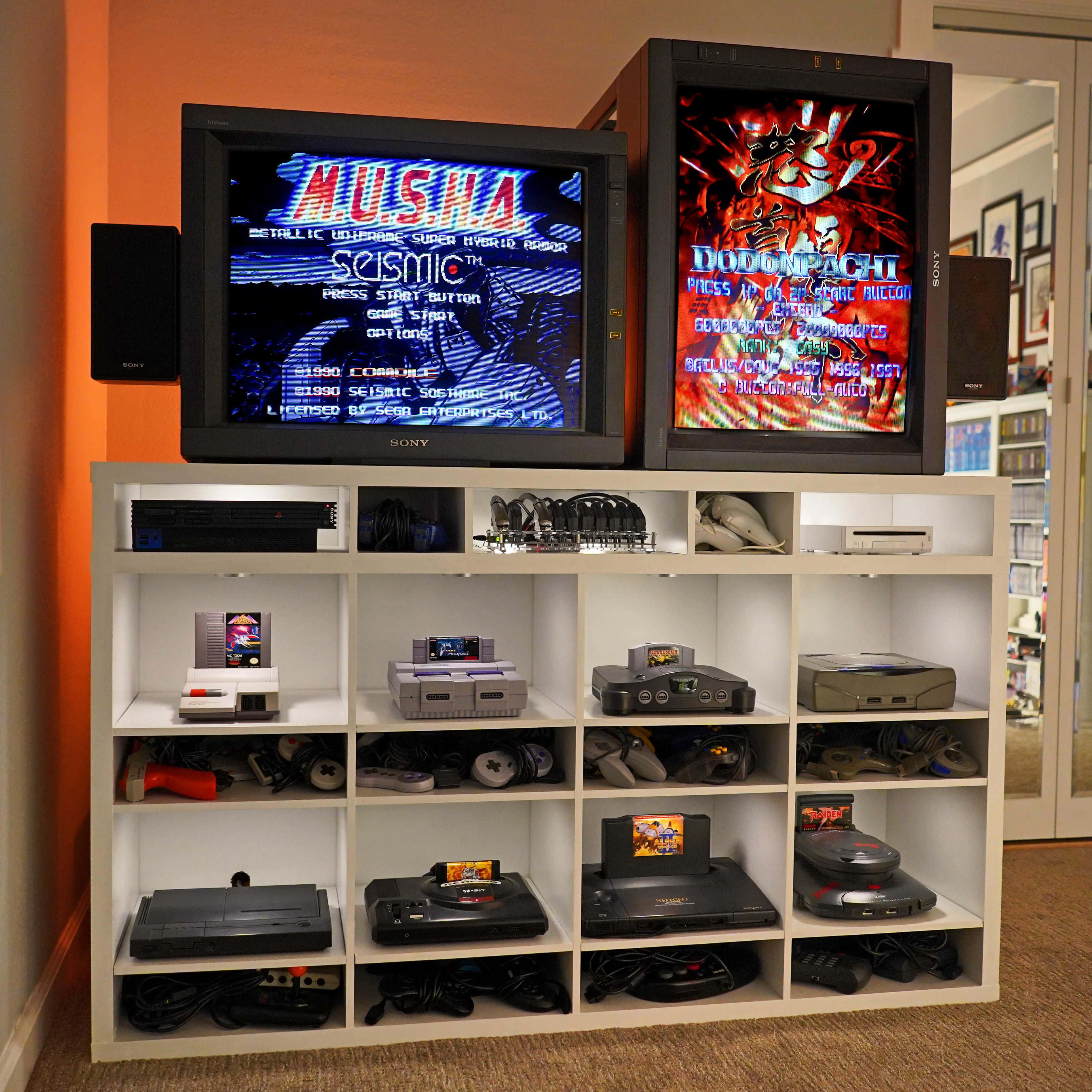 Game Console Emulators 桌布 壁紙 — 兩部復古CRT電視在一個裝滿經典遊戲主機和手把的白色層架上方顯示復古街機遊戲。