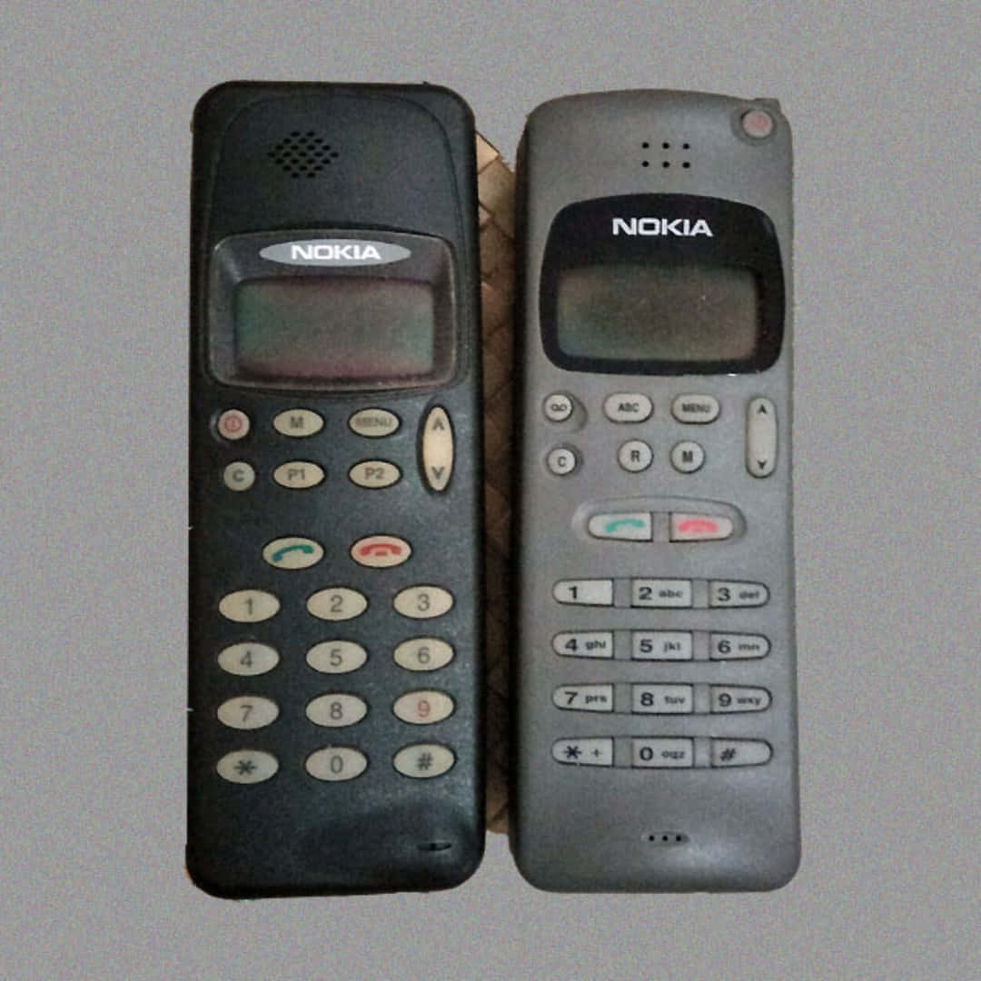 手機 桌布 壁紙 — 兩部復古Nokia無線電話黑色和灰色並排靠在素牆上，牆上顯示出老化和使用痕跡。