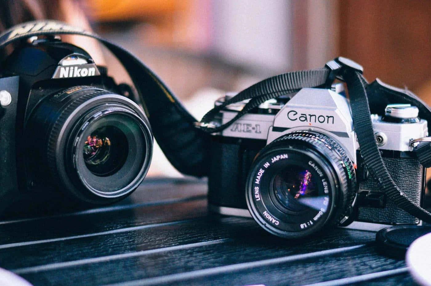 相機 桌布 壁紙 — 兩部復古相機Nikon和Canon並排放在深色木質表面上，搭配柔和溫暖的燈光。