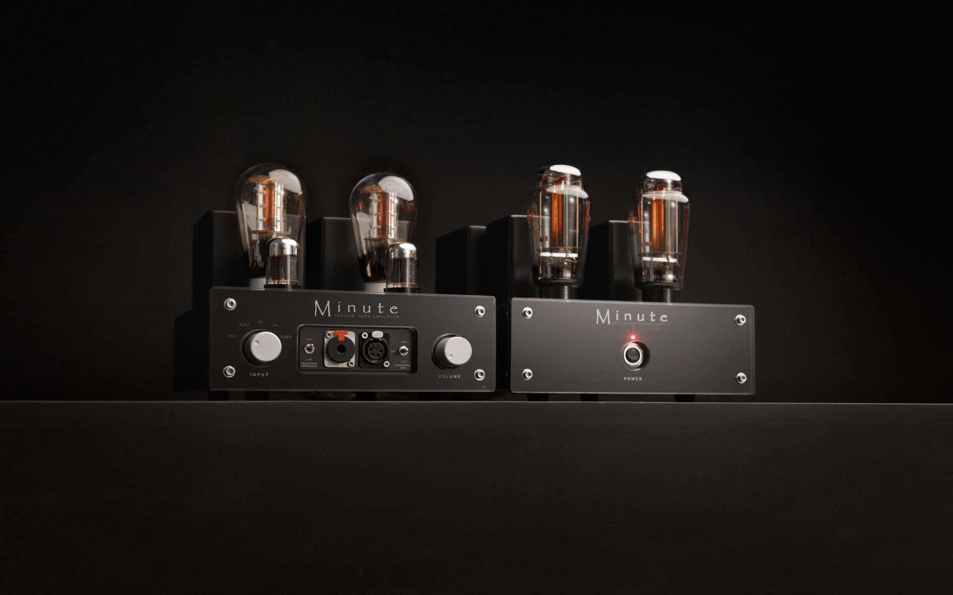 Guitar Amp 桌布 壁紙 — 兩部時尚黑色 Minute 音頻放大器，帶有發光的真空管，立在深色背景前。