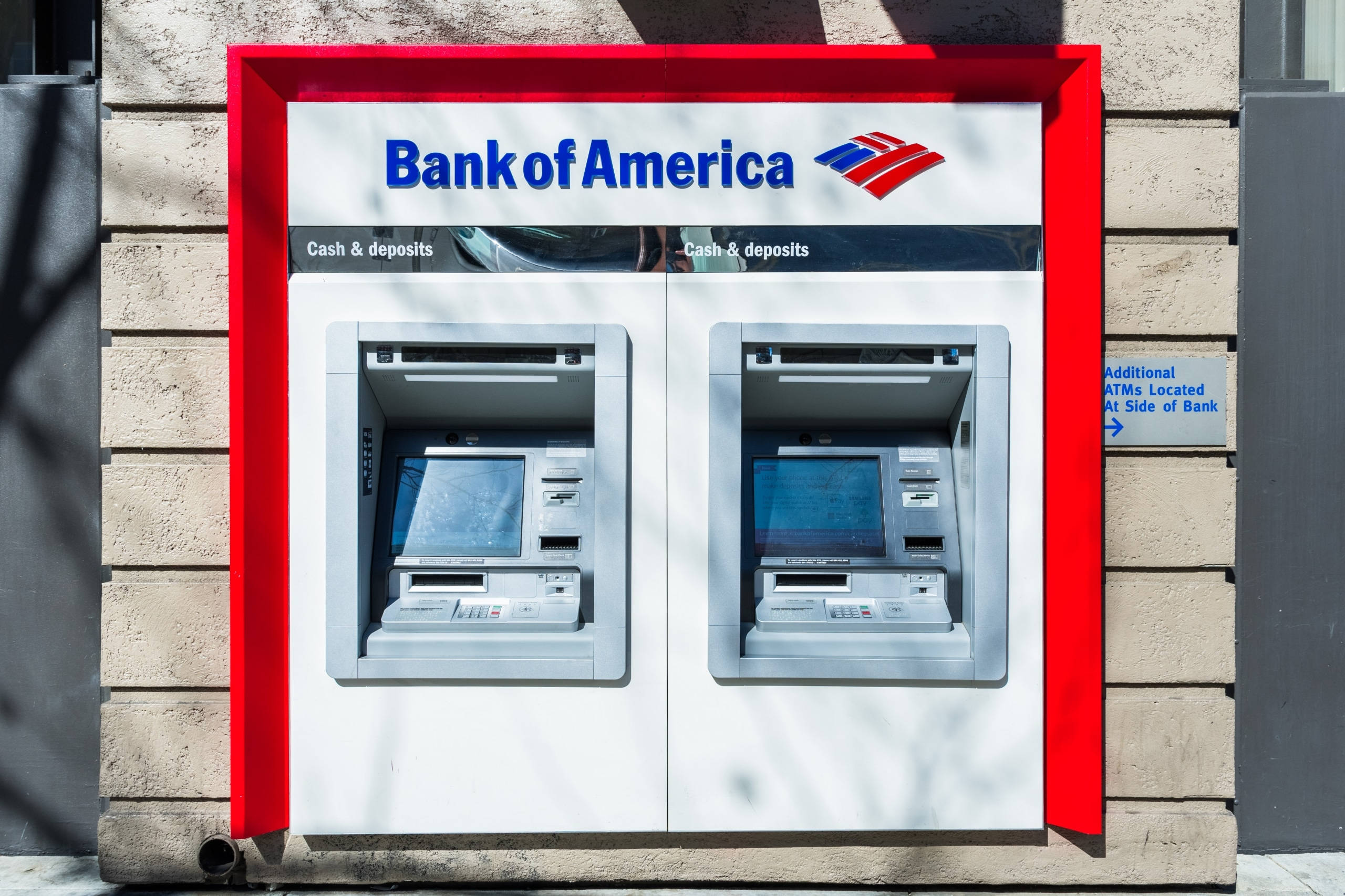 Bank 桌布 壁紙 — 兩部美國銀行自動櫃員機位於一個紅色框架的亭子內，安裝在米色磚牆上，在明亮的日光下。