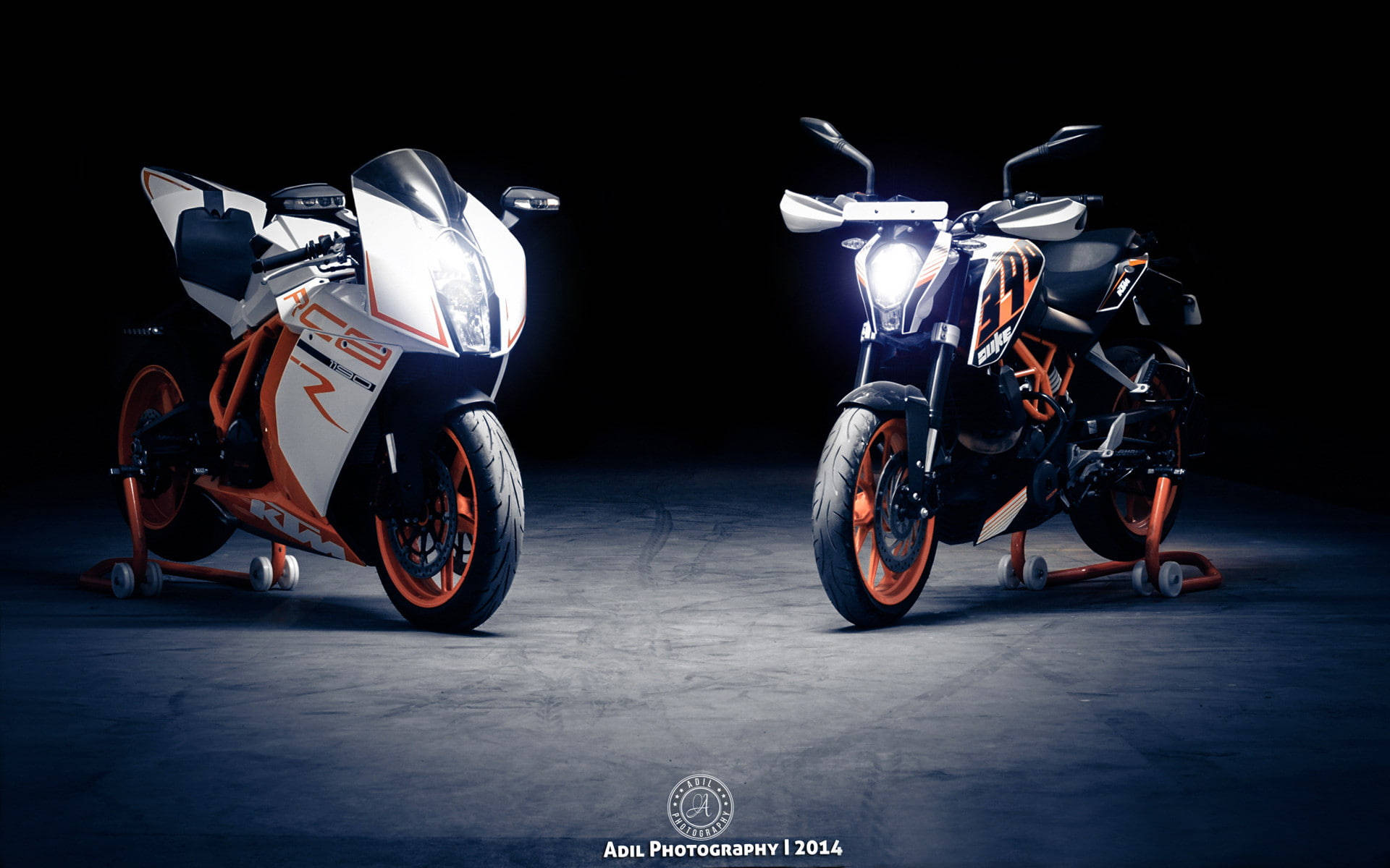 KTM 摩托車 桌布 壁紙 — 兩部高性能KTM機車，車頭燈閃爍，在漆黑的攝影棚背景下戲劇性地照亮。