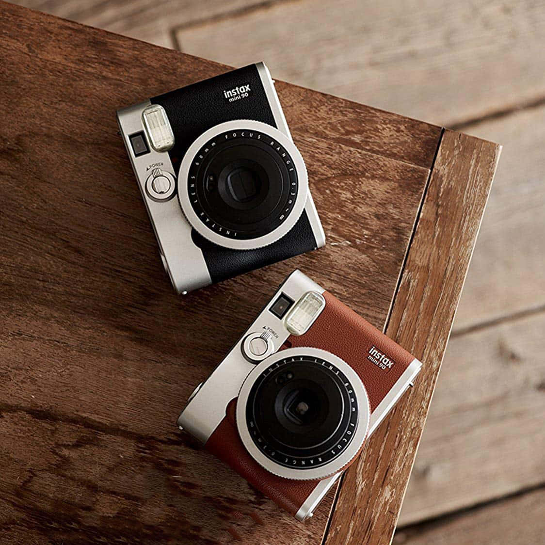 相機 桌布 壁紙 — 兩部黑色和棕色皮革的Instax Mini 90即時相機放在質樸的木質表面上。