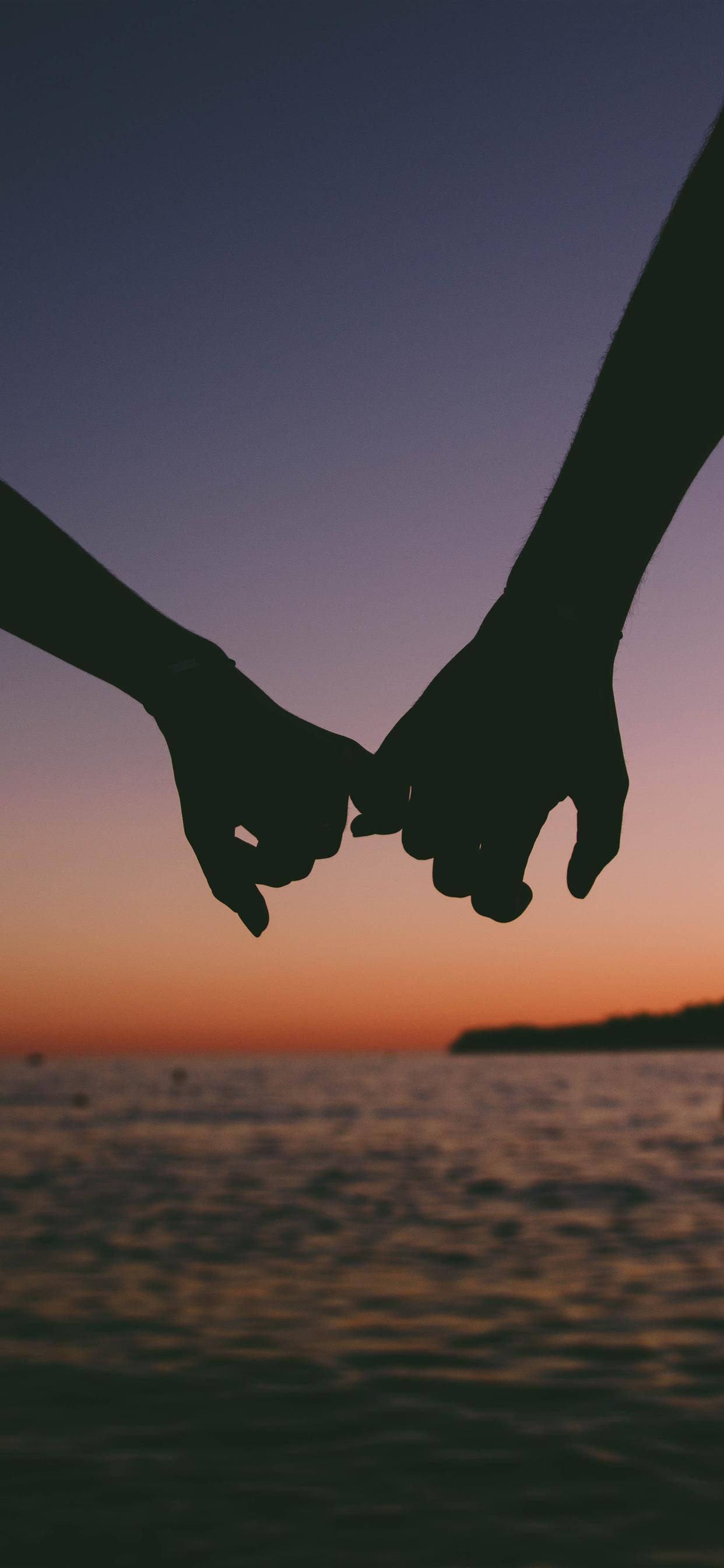 Love iPhone 桌布 壁紙 — 兩隻剪影的手在平靜水面上燦爛的日落中緊握在一起。