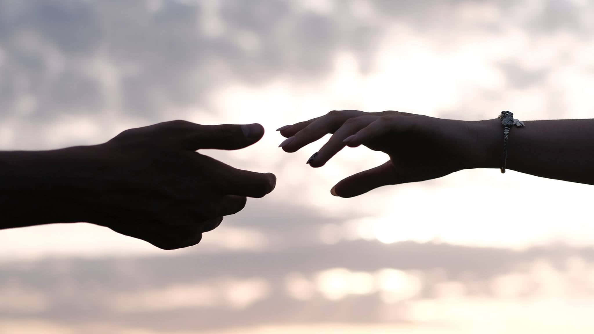 Sunlight 桌布 壁紙 — 兩隻剪影般的手在日落時分柔和發光的天空下互相伸向對方。