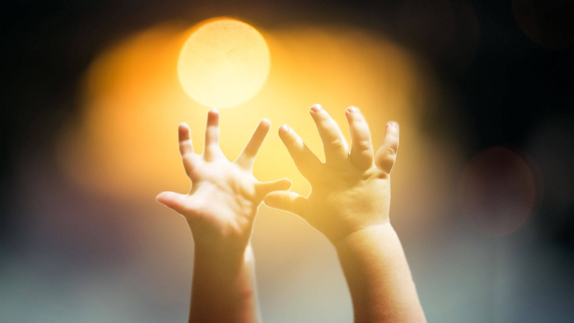 太陽 桌布 壁紙 — 兩隻小手伸向一個在黑暗模糊背景中發光的金色球體。