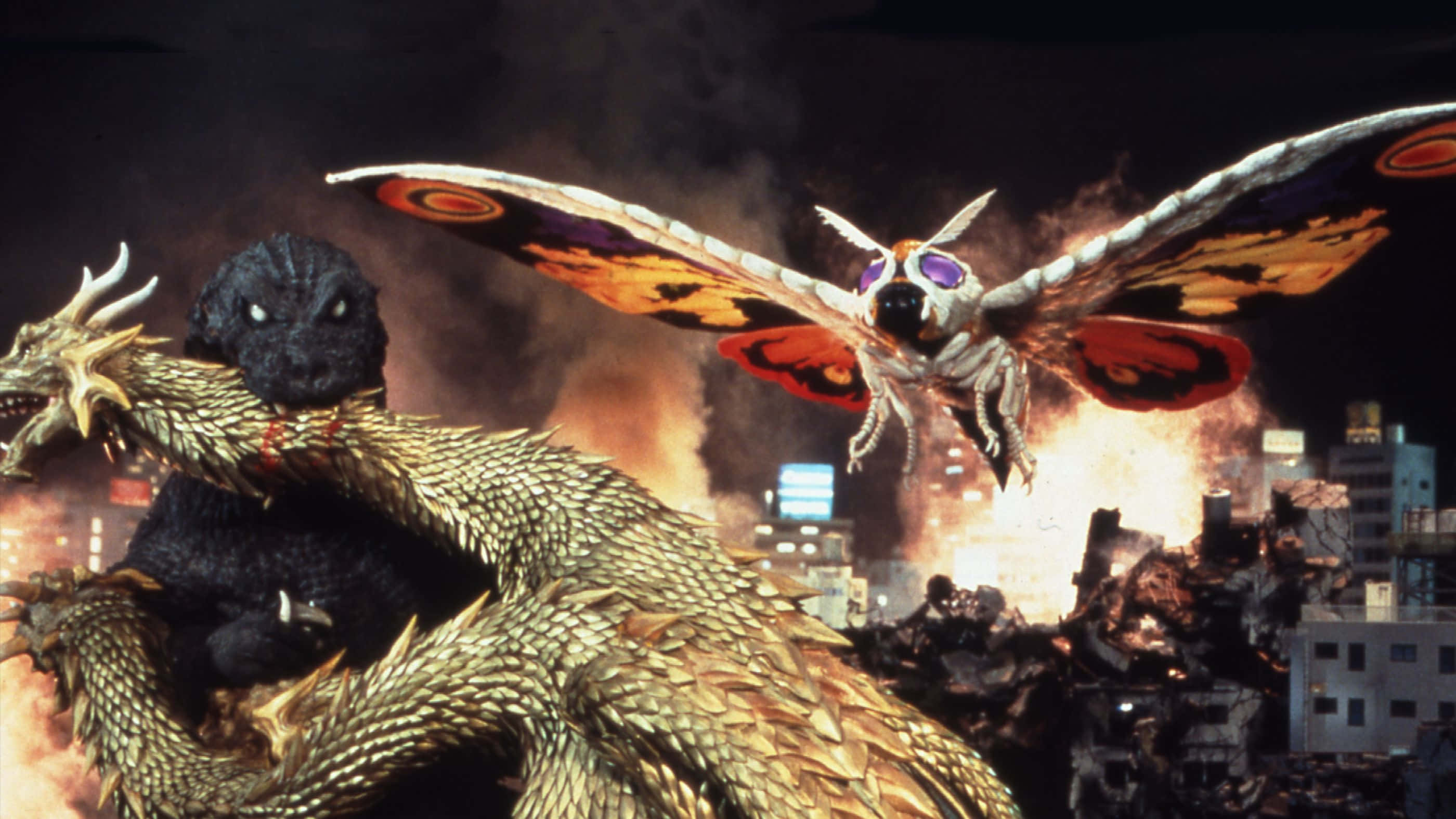 Godzilla Vs Mothra 桌布 壁紙 — 兩隻巨型怪獸哥吉拉和摩斯拉在爆炸和煙霧中，於燃燒的城市景觀中戰鬥。