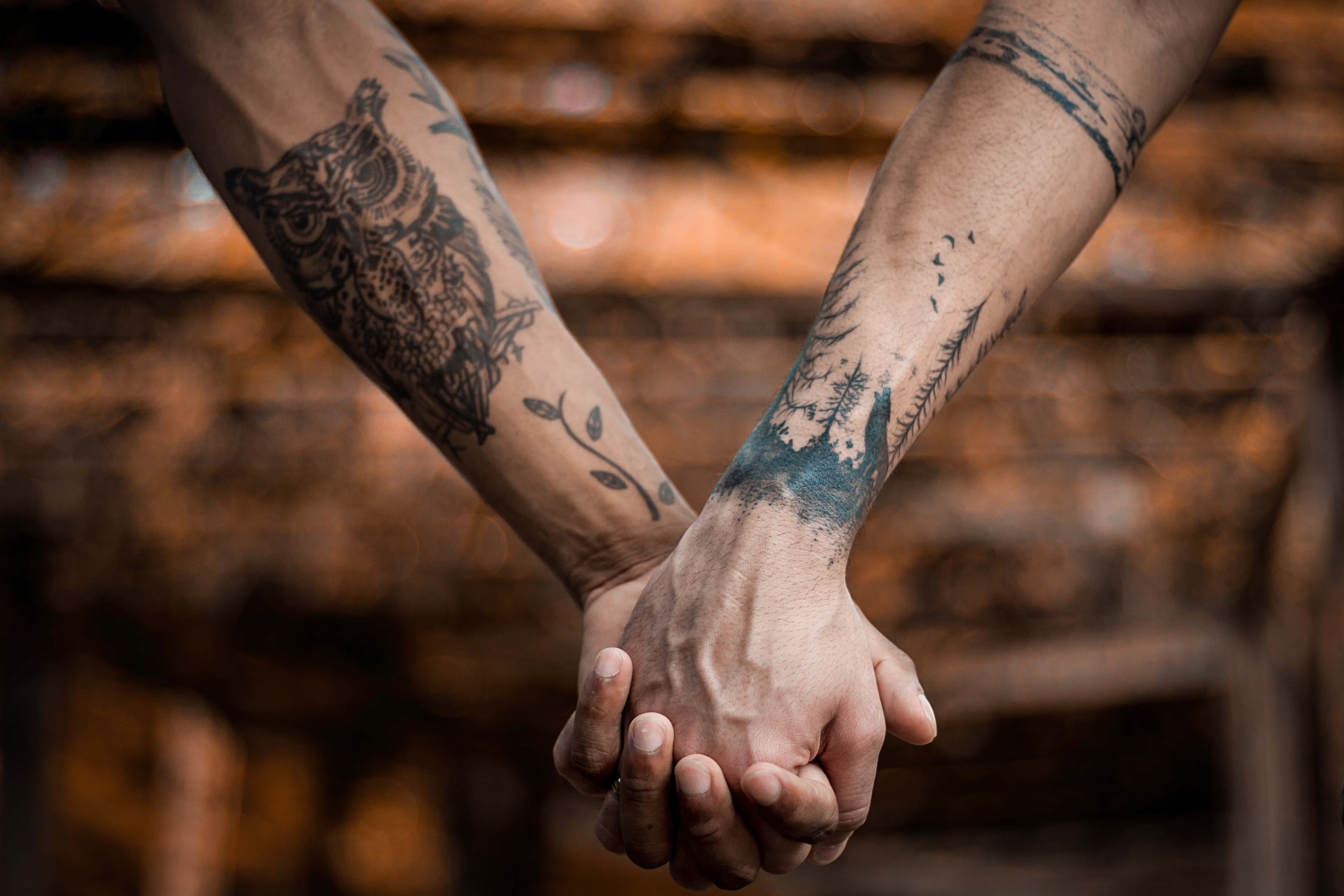 hands 桌布 壁紙 — 兩隻帶有刺青的手臂在溫暖模糊的木質背景前交握雙手。
