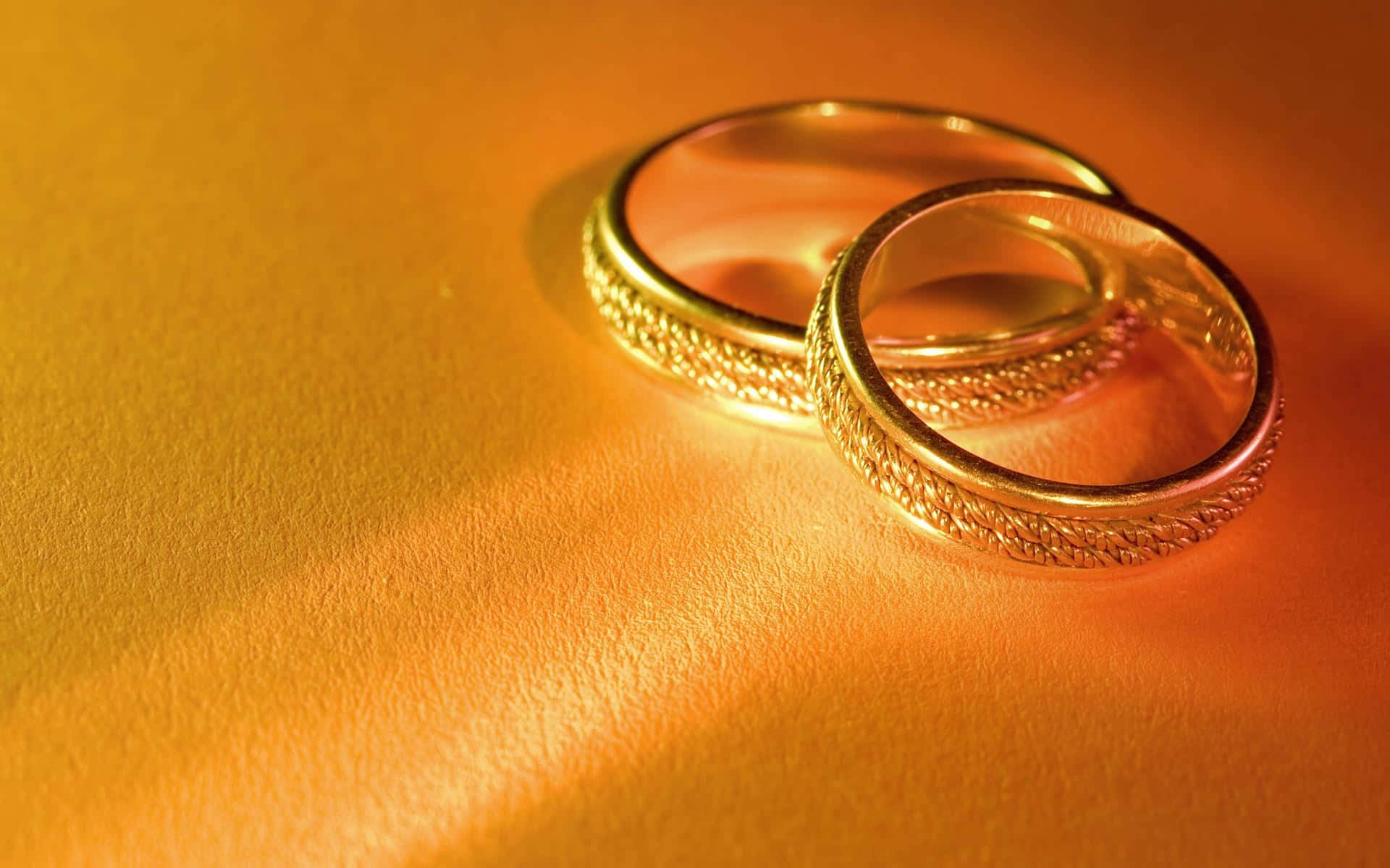 Ring 桌布 壁紙 — 兩隻帶有紋理的金色結婚戒指，放置在溫暖的金色表面上，沐浴在柔和的方向光中。