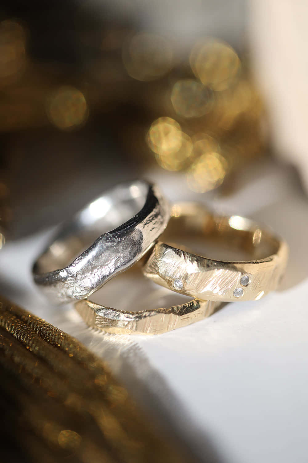 結婚戒指 桌布 壁紙 — 兩隻帶紋理的結婚戒指，一銀一金，放在白色表面上，背景為金色散景。